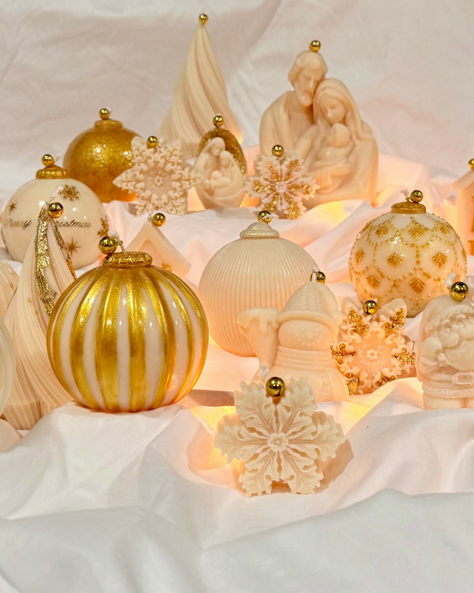 Decorative Christmas ornaments and figurines on white fabric, including a nativity scene, snowflakes, and gold accents.