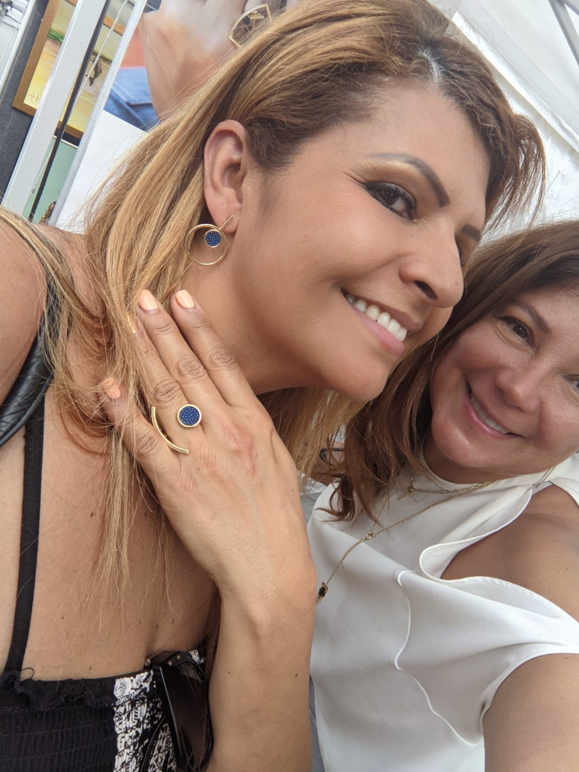 Two women smiling, one showing a ring on her finger, with a window in the background.