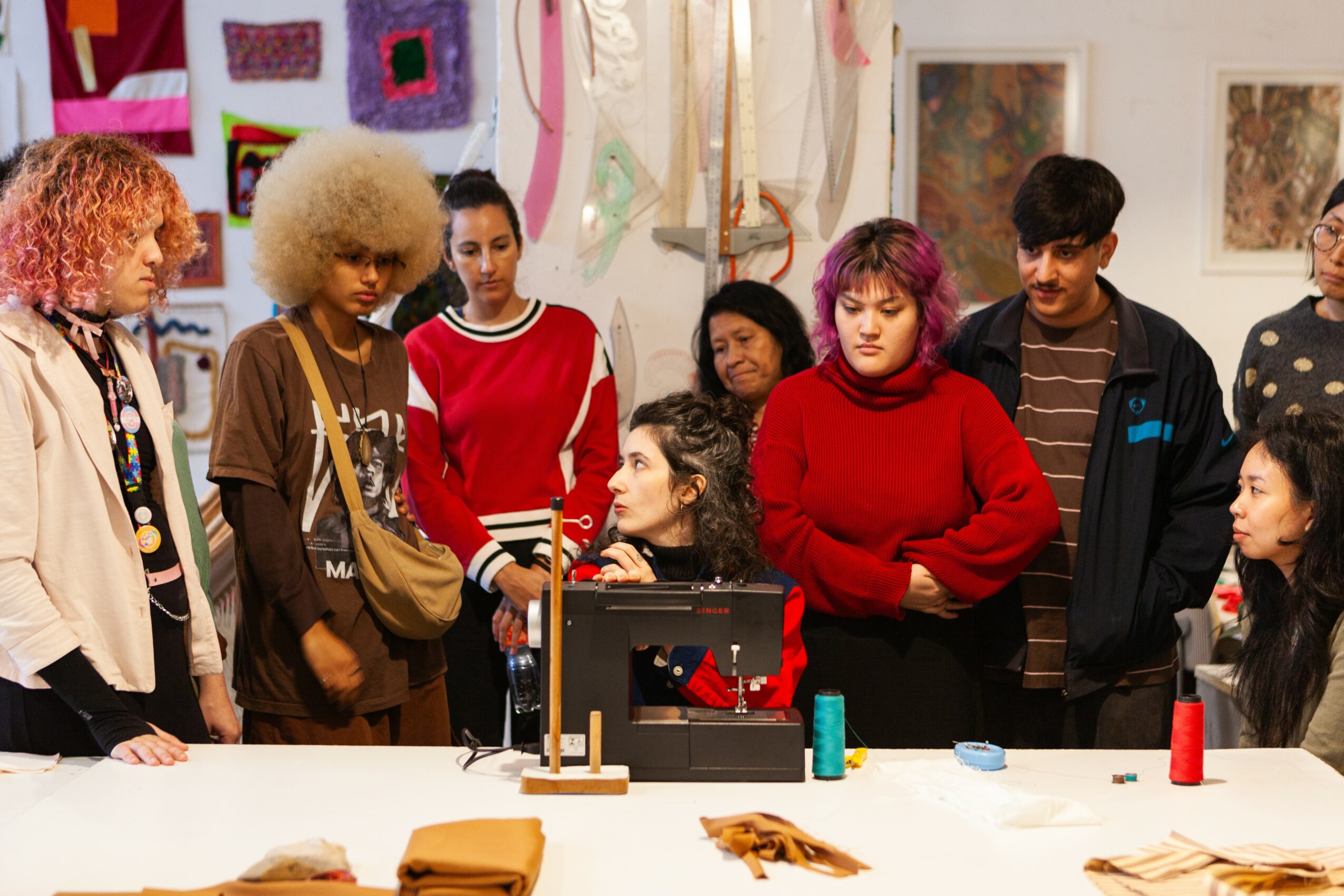 Group of diverse people gathered around a table in an art studio, engaging in a discussion or workshop.