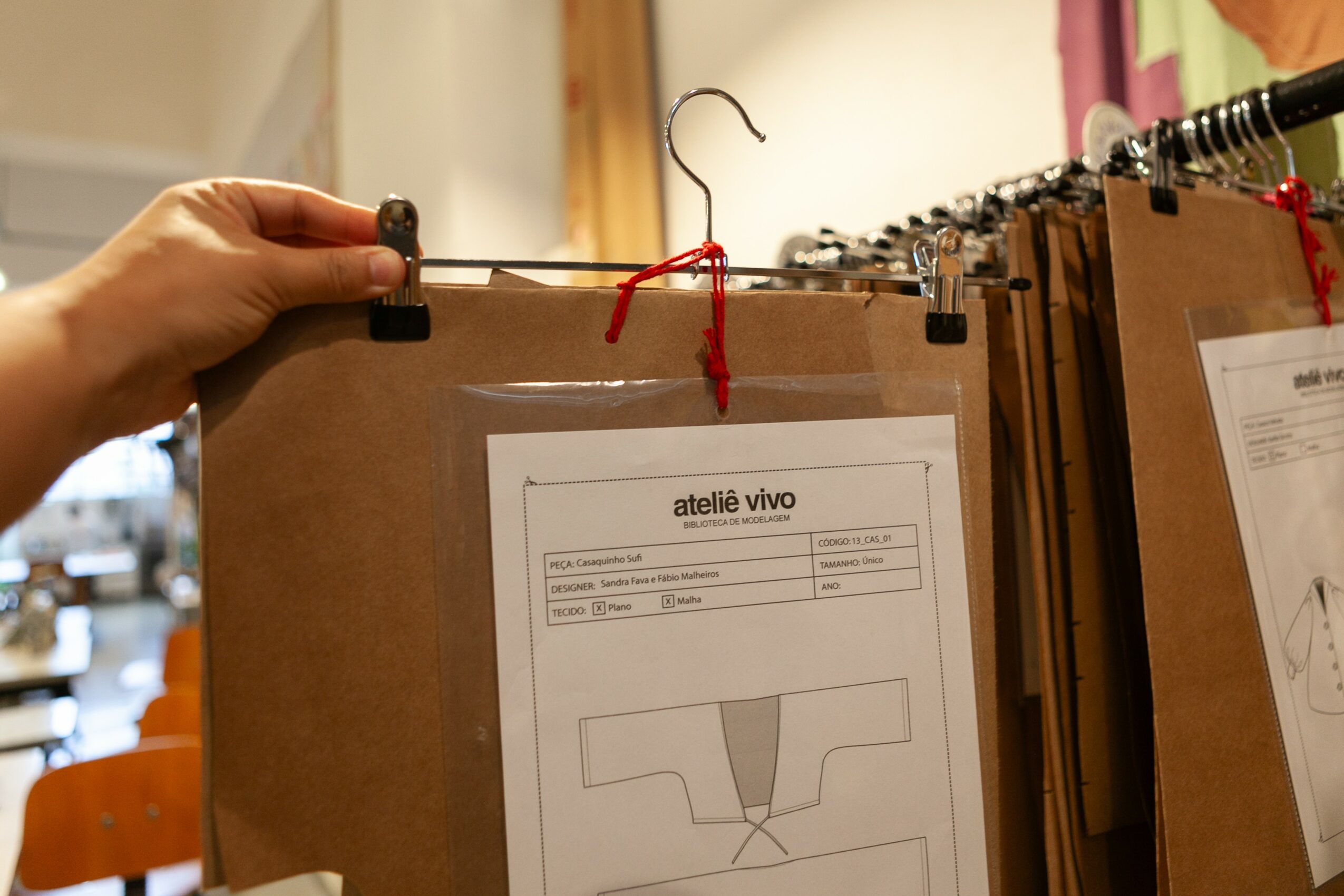 Hand holding a clipboard with a paper, hanging among other clipboards on a rack, in a room with wooden furniture.