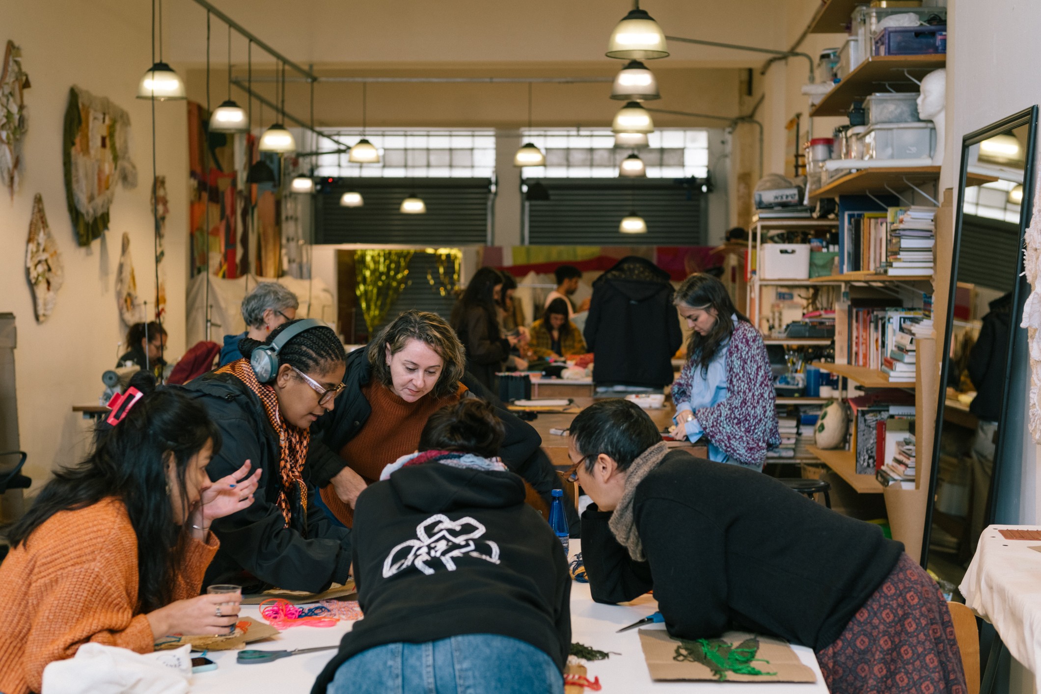 Group of people working together at a table in a room with shelves and artwork, some wearing headphones.