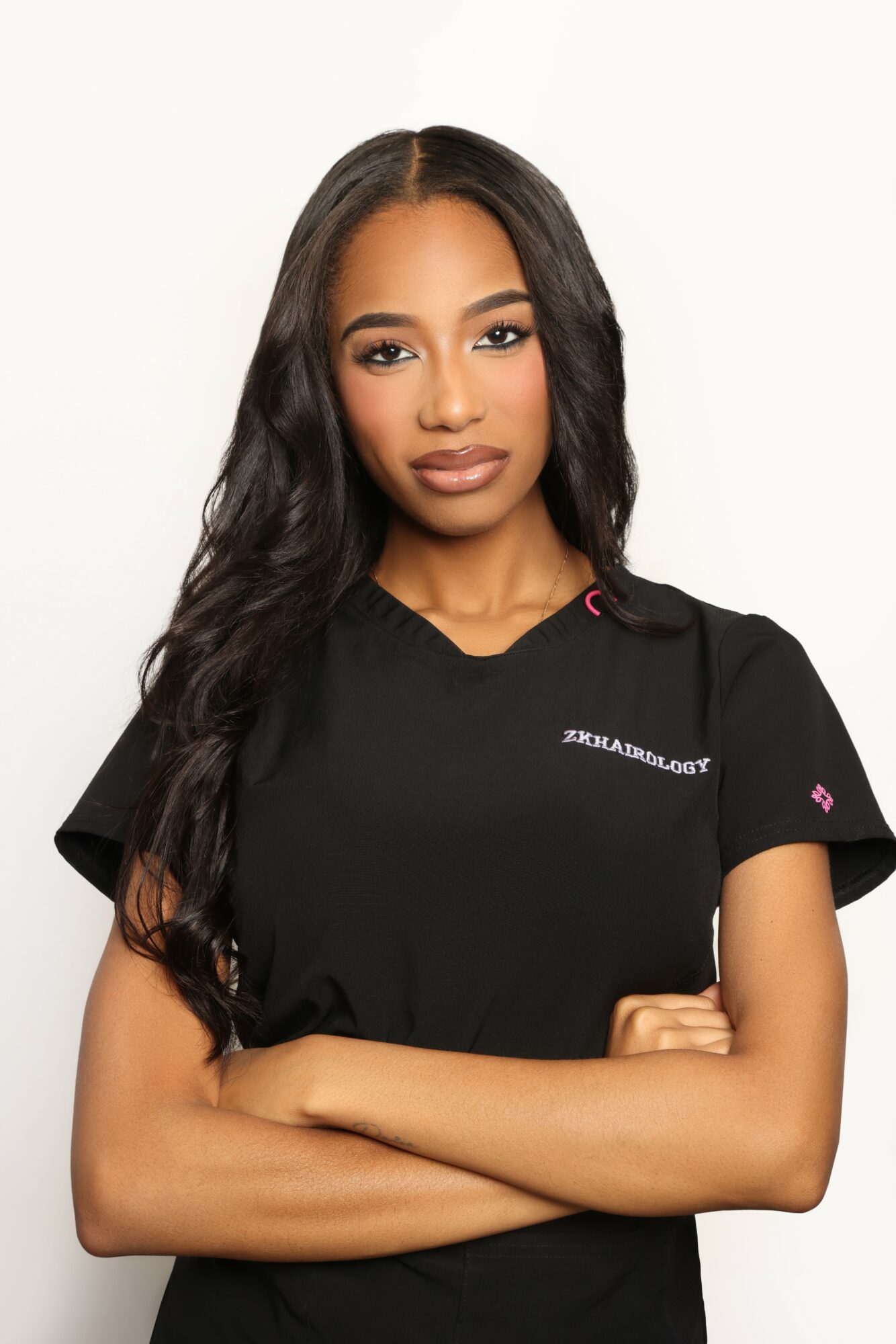 Young woman with long wavy hair wearing a black shirt, arms crossed, neutral expression, plain white background.