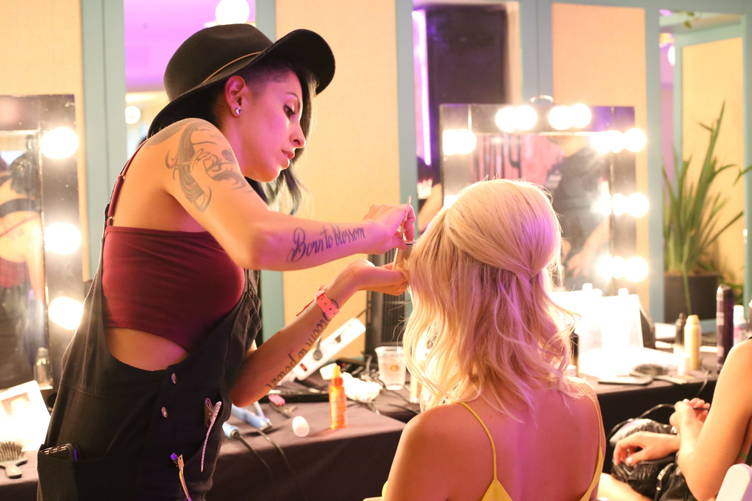 Makeup artist applying makeup to a woman with blonde hair in a brightly lit room.