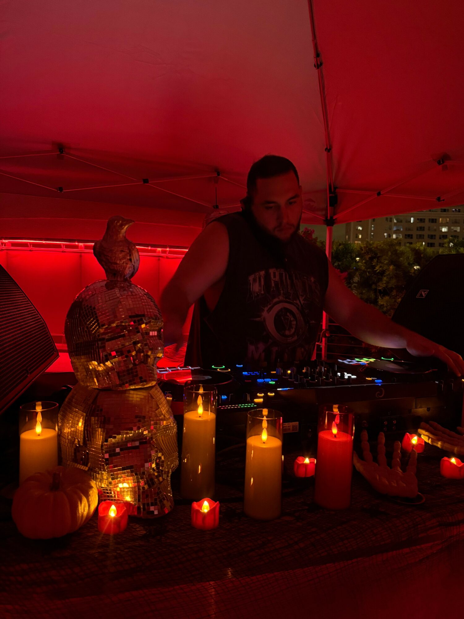 Person standing behind a bar with bottles and candles, in a dimly lit setting with red lighting.