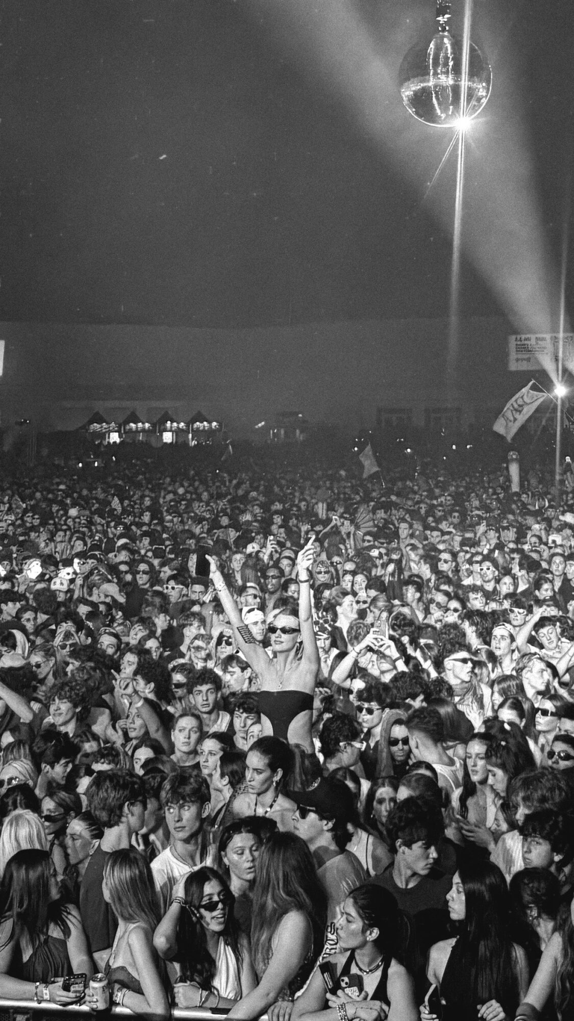 Crowd at a concert with a disco ball hanging from the ceiling, people dancing and enjoying the event.