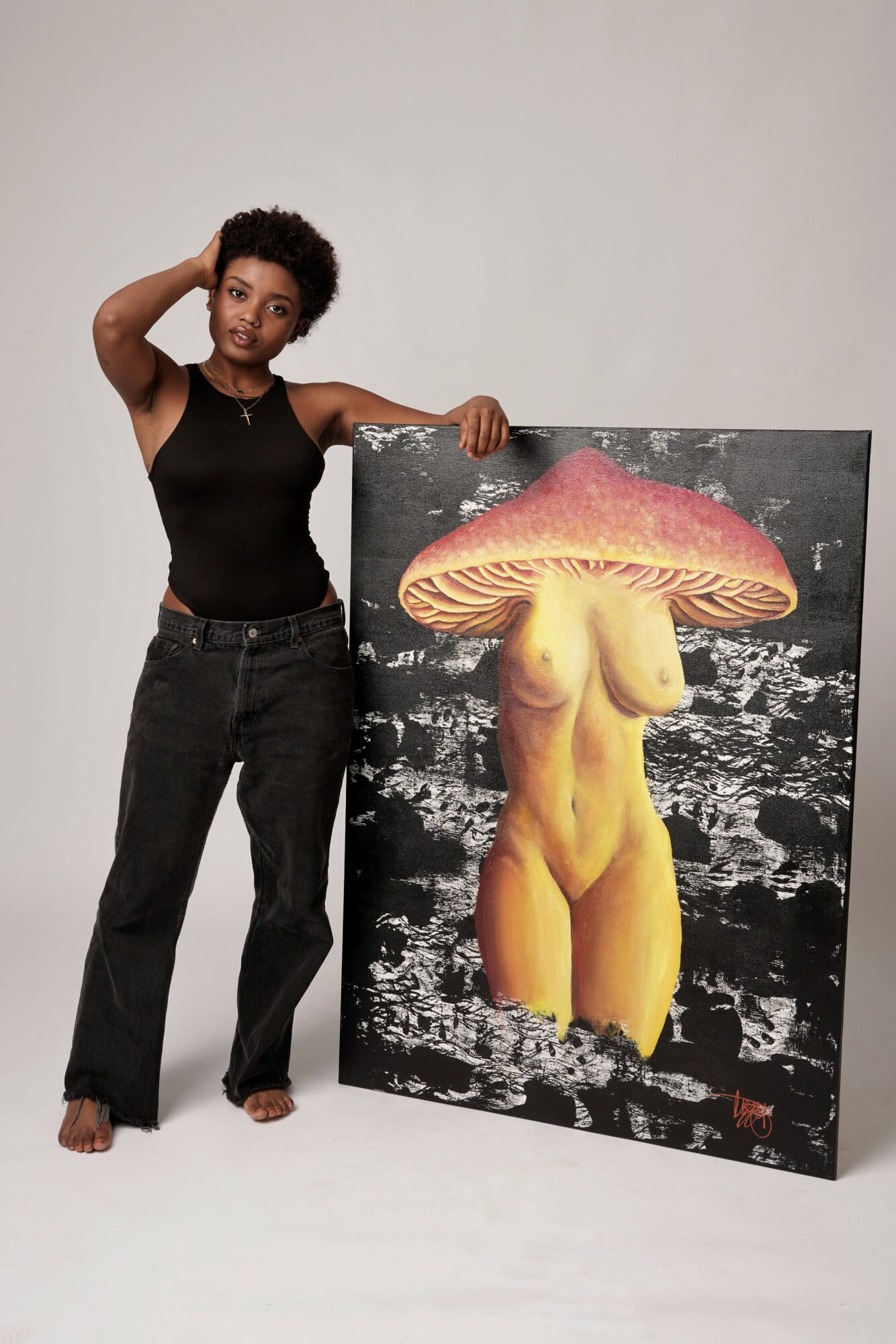 Woman standing next to a painting of a figure with a mushroom cap as a head and a nude body, on a plain background.