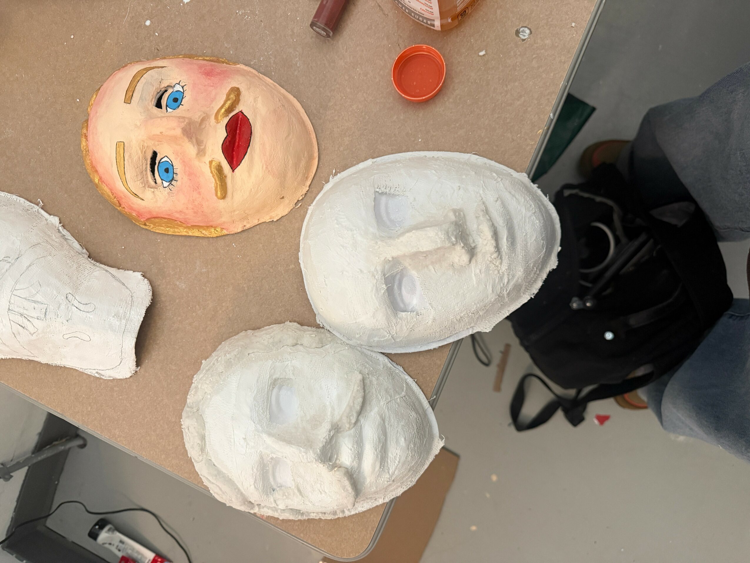 Three white masks and a painted face mask on a table, with makeup items nearby.
