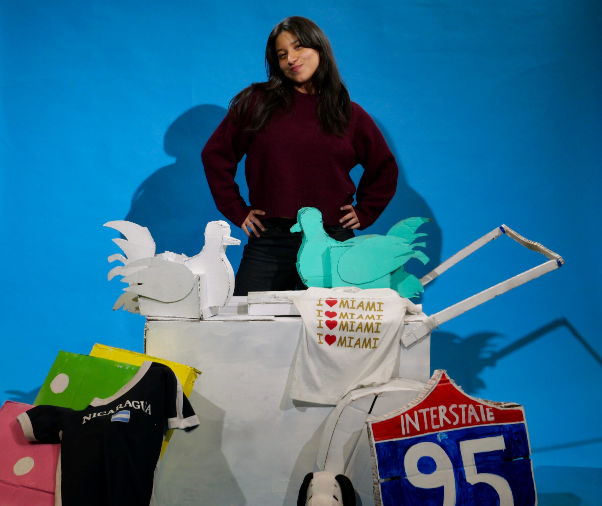 Woman standing behind a cart with paper cutouts of animals and signs, against a blue background.