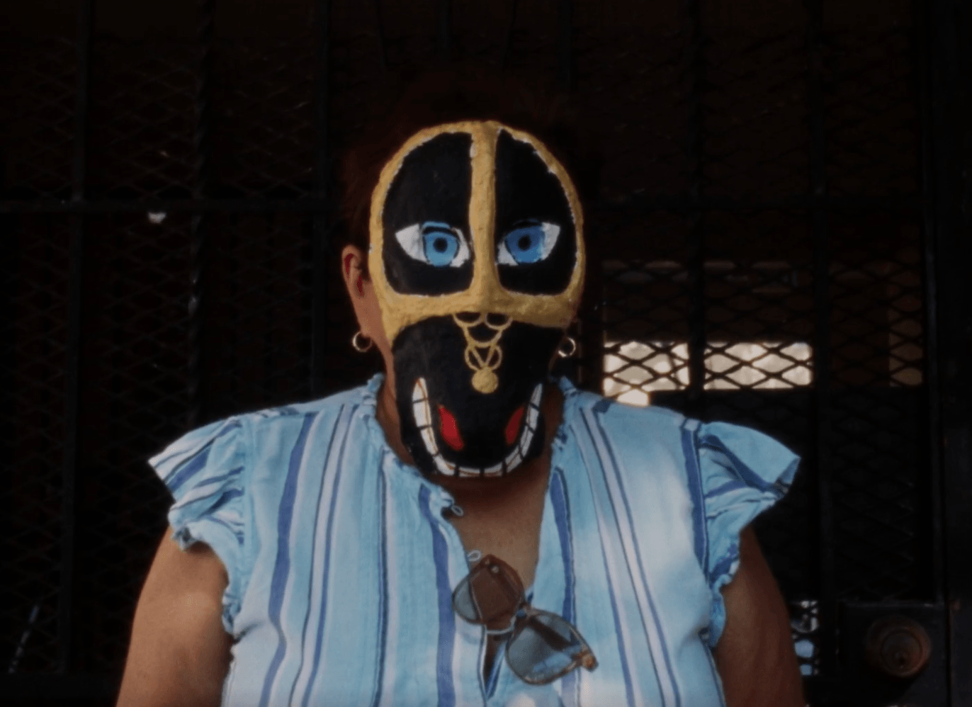Person wearing a black and yellow mask with blue eyes, black nose, and open mouth, dressed in a striped shirt.