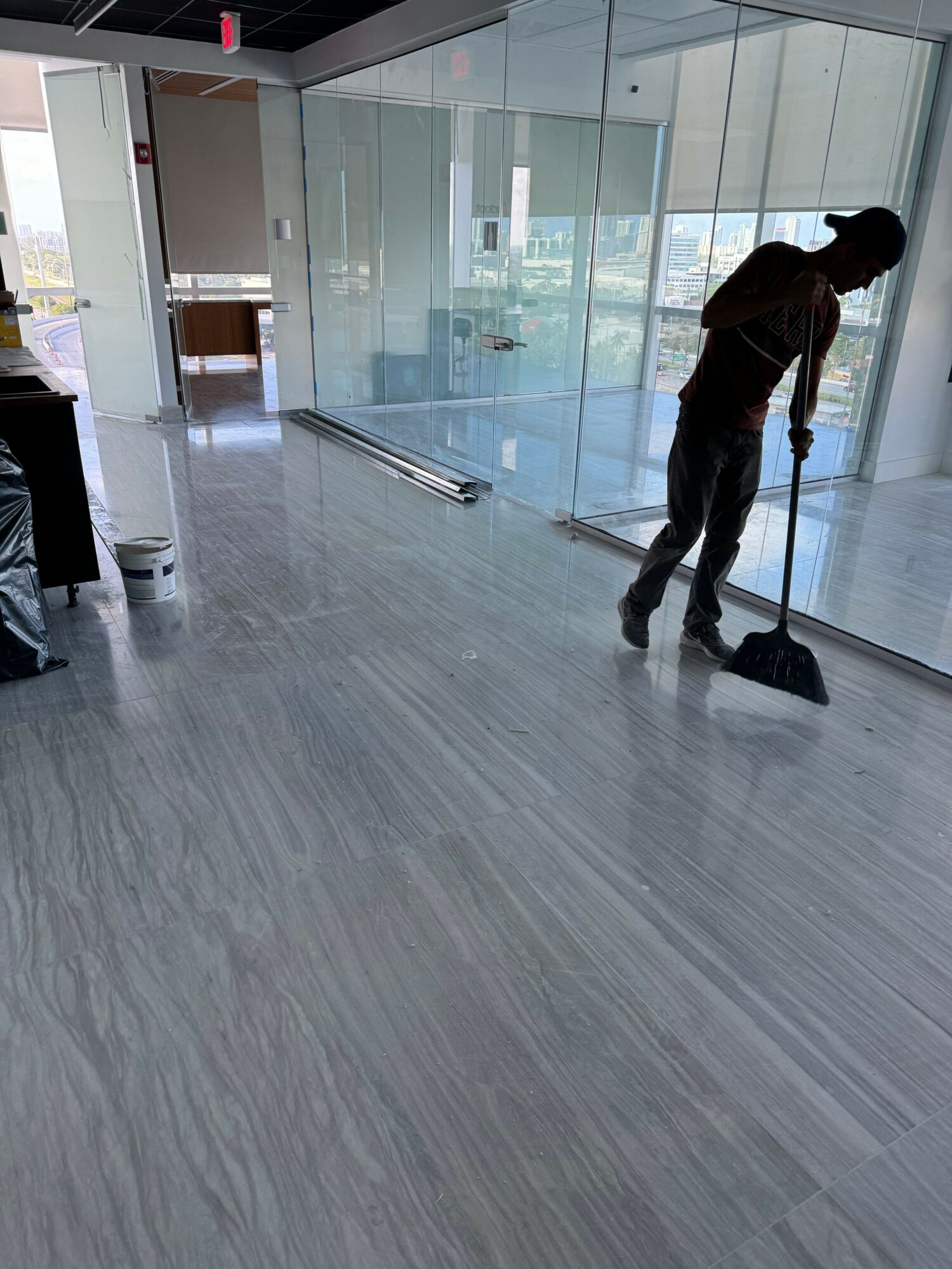 Person cleaning floor with a mop in a modern indoor space, glass walls, and natural light.