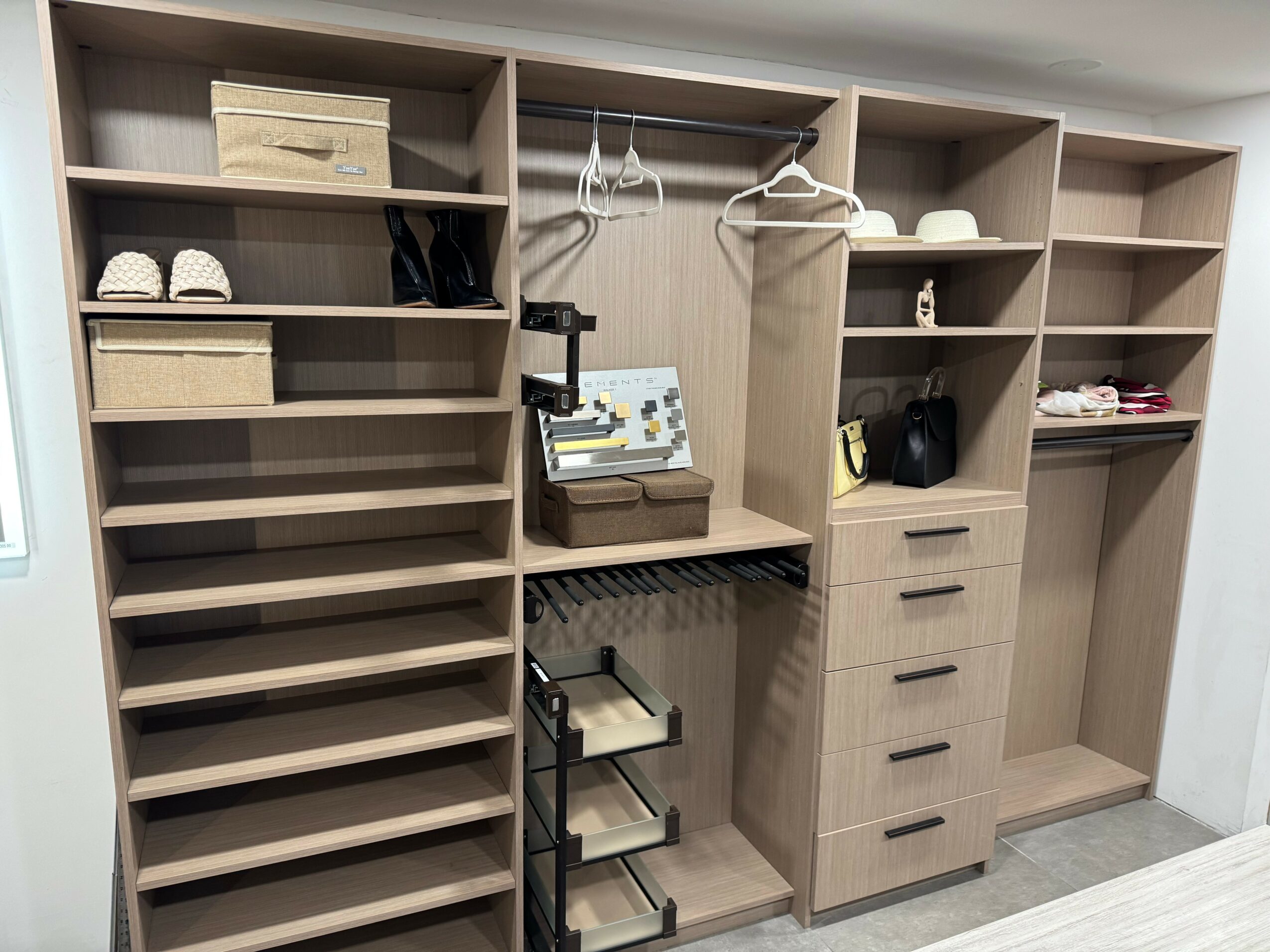 Empty wooden closet with shelves, drawers, and hanging space, with some shoes and bags inside.