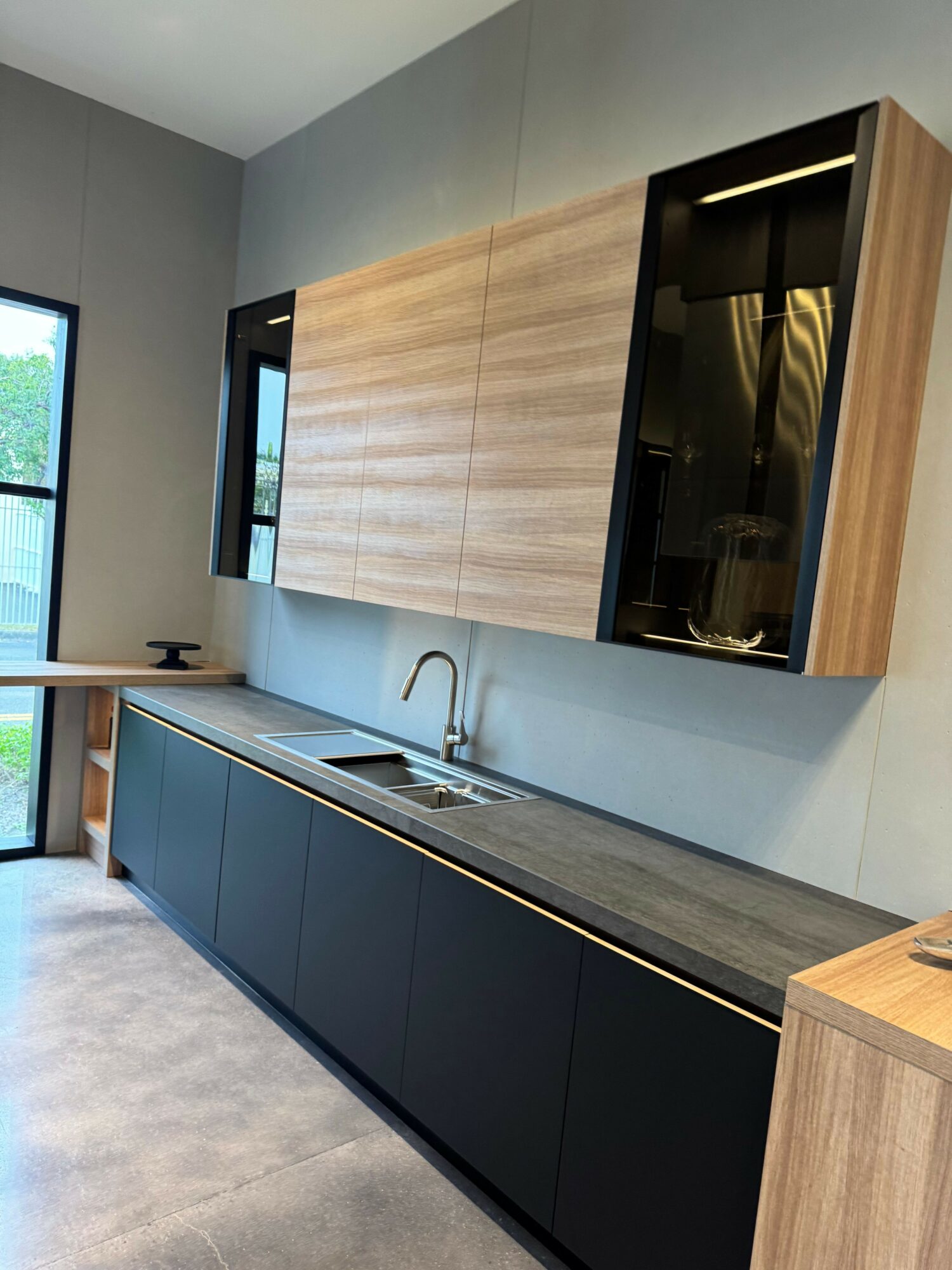 Kitchen with wooden cabinets, black appliances, and a gray countertop, viewed from the side with a window and sink.