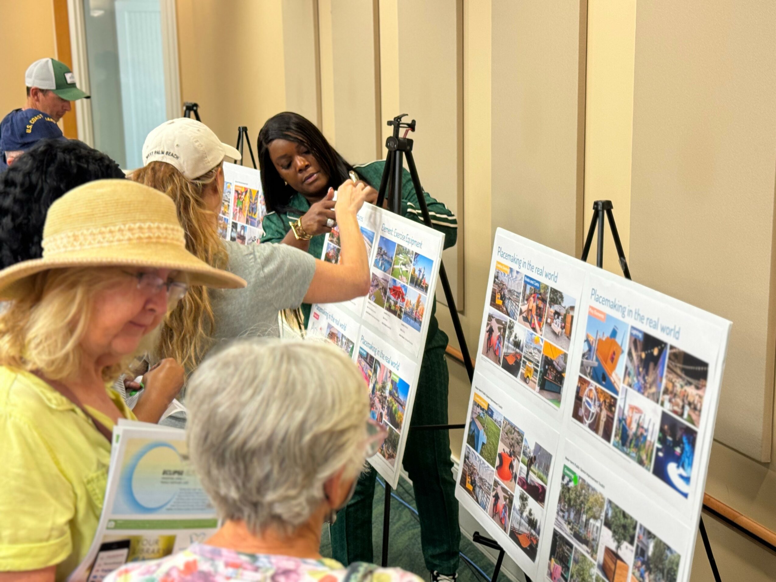 Group of people, including children and adults, viewing and discussing colorful display boards at an indoor event.