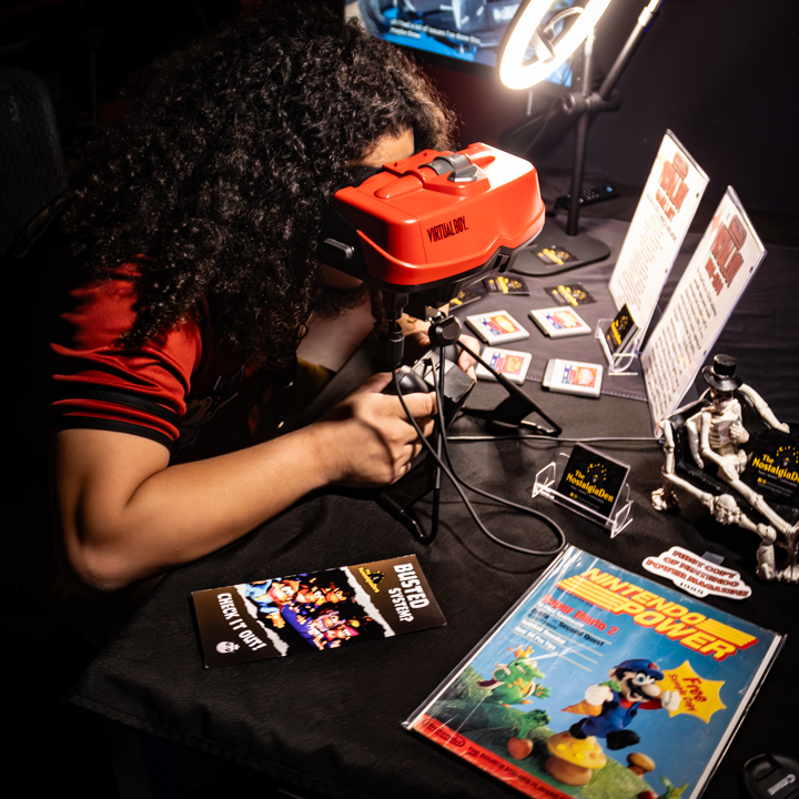 Person using a virtual reality headset at a table with gaming items and promotional materials.