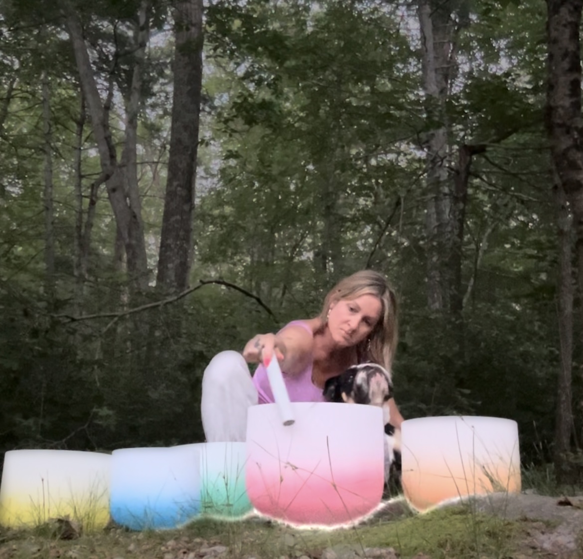 A woman with long hair in a pink top is outdoors among trees, surrounded by colorful large cups or containers.