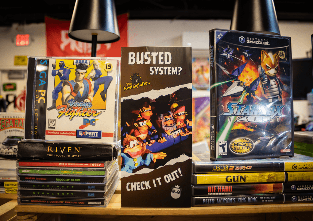 Shelf with video game cases, a comic book, and a poster, with black pendant lights above. The poster features characters from a game.