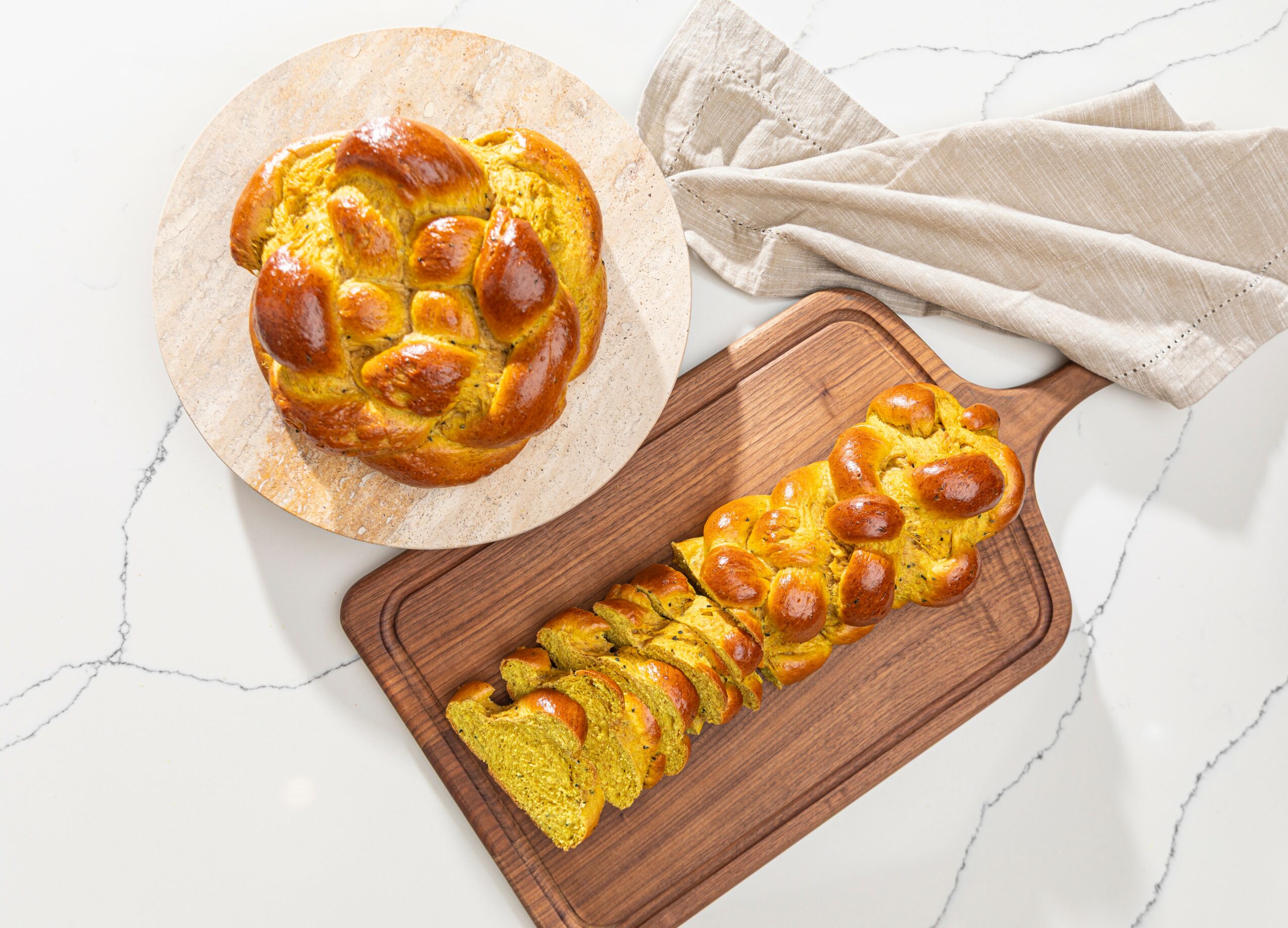 Round bread topped with cheese and sausage slices on a wooden board, sliced into pieces, on a white surface with a cloth.