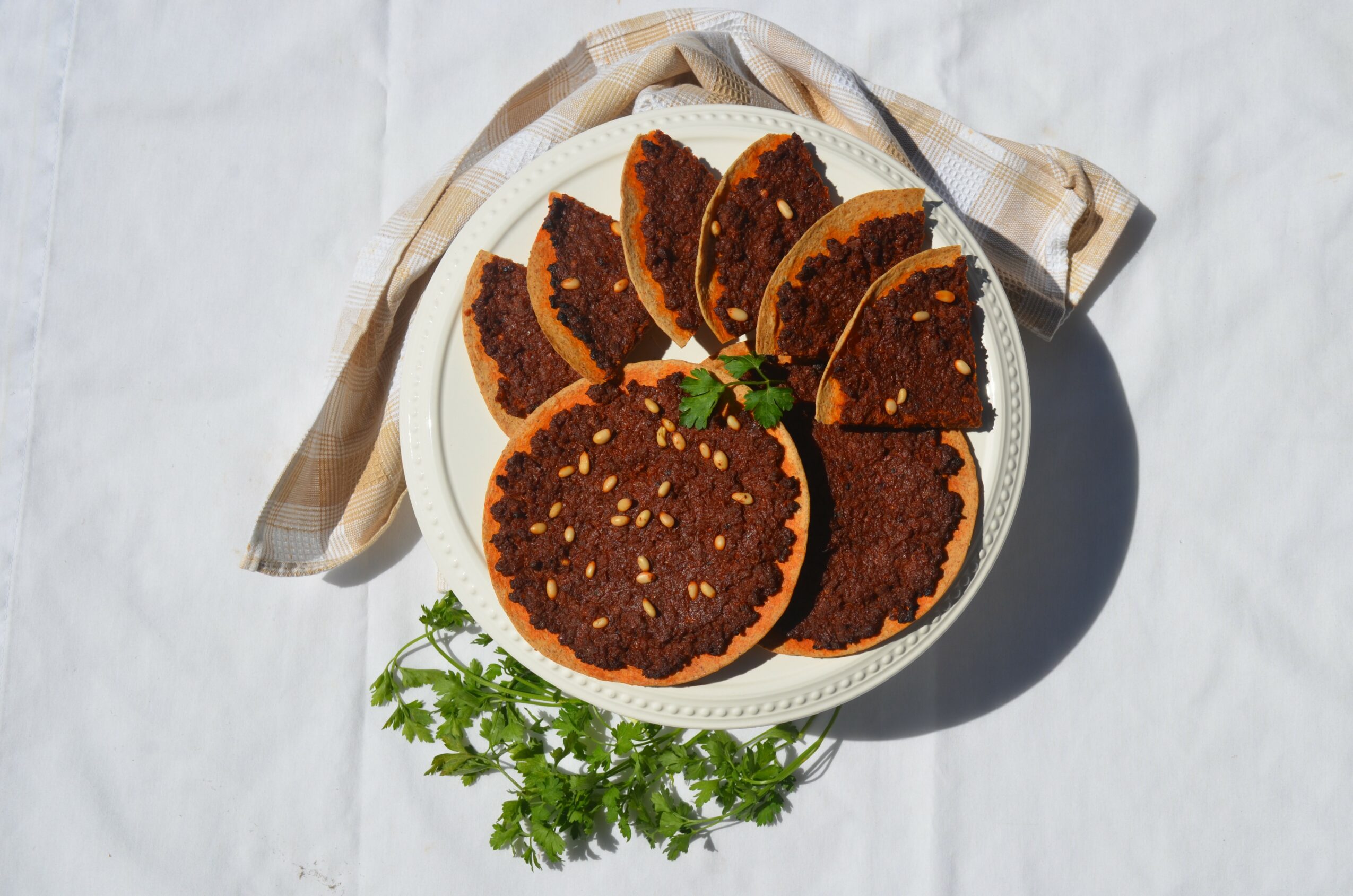 Plate with sliced dark brown snack items, some with sesame seeds, on a white surface with a cloth and green garnish.