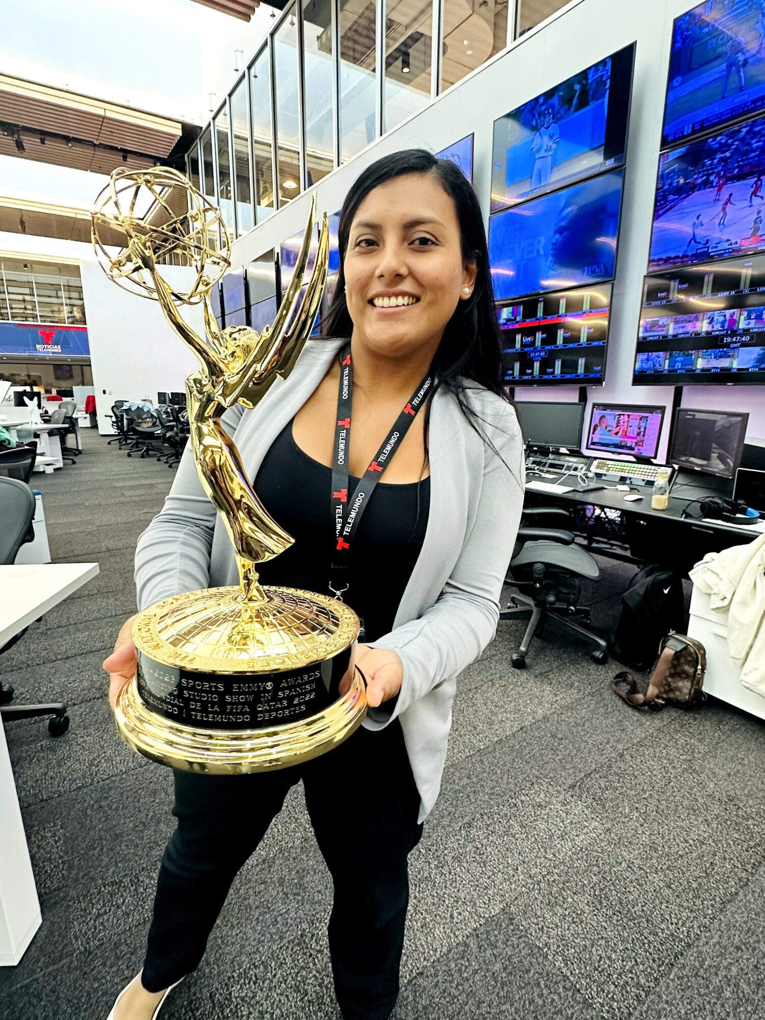 Woman holding a large award trophy in an indoor setting with screens and equipment behind her.