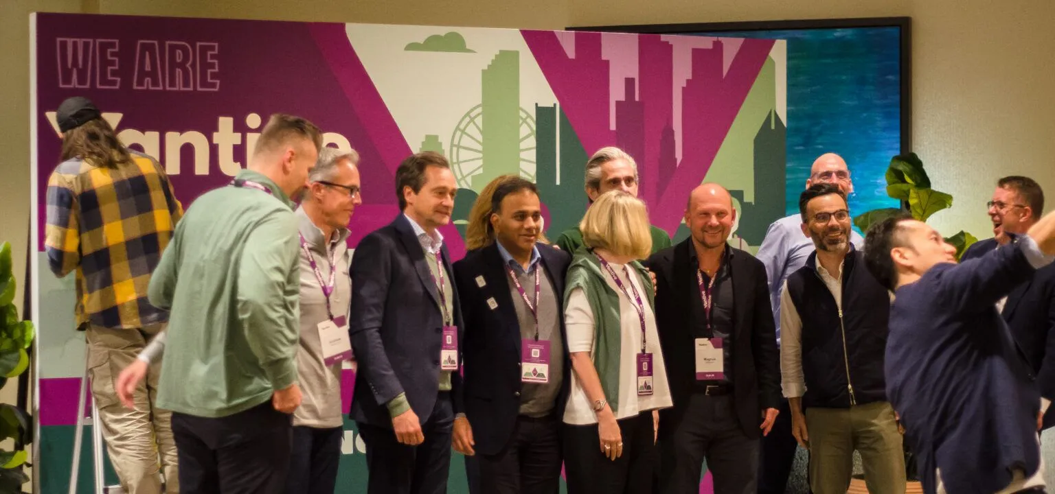 Group of people standing together at an indoor event, with a colorful cityscape background and a large sign reading 'WE ARE' and 'NYC'.