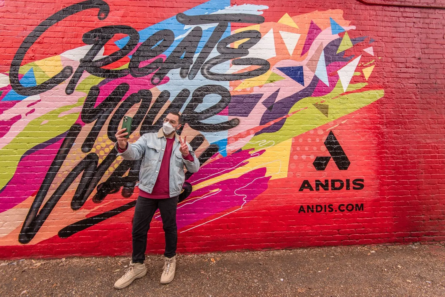 Person standing in front of colorful graffiti wall, holding a phone, wearing a backpack and sunglasses.
