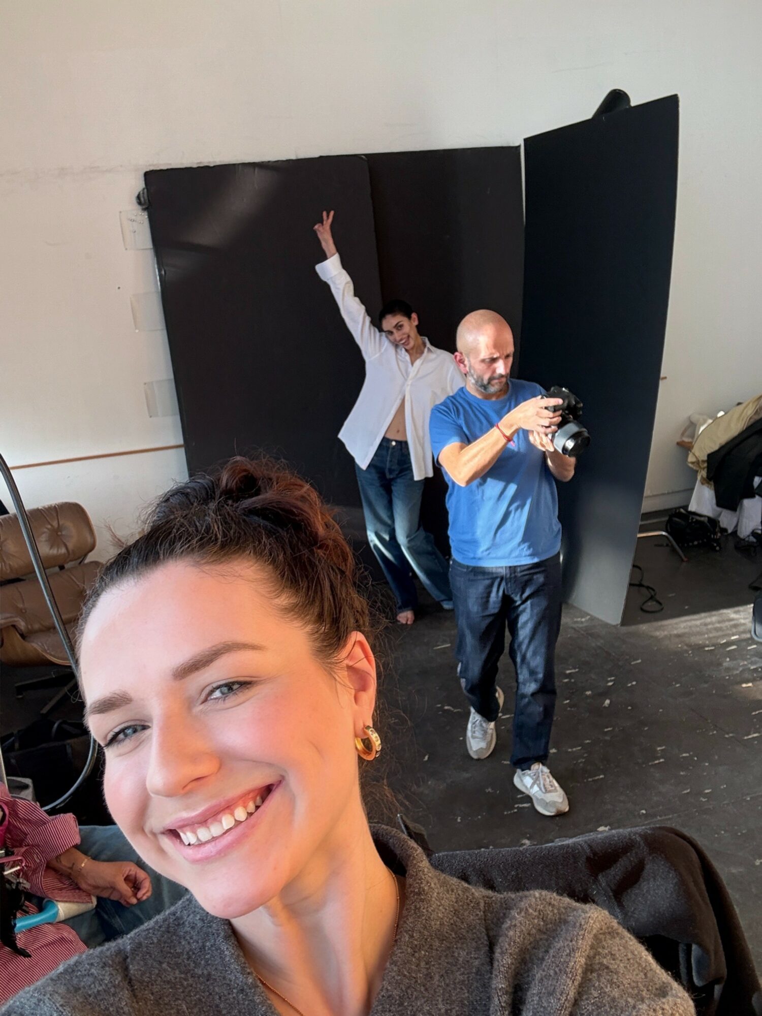 Smiling woman in foreground with two men in background, one holding a camera, in a studio setting.