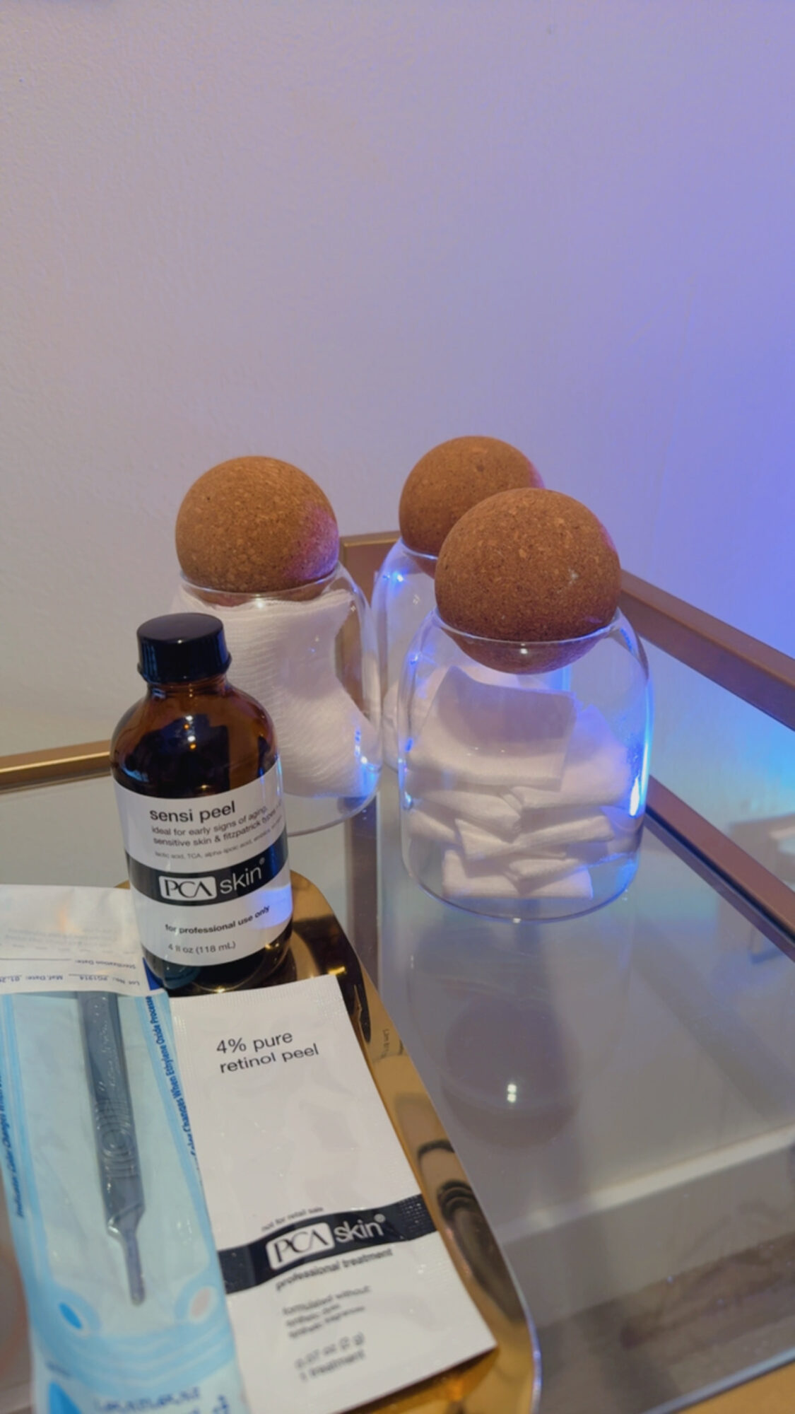 Three glass jars with round brown objects on top, a small dark bottle, and a paper with text on a glass surface.