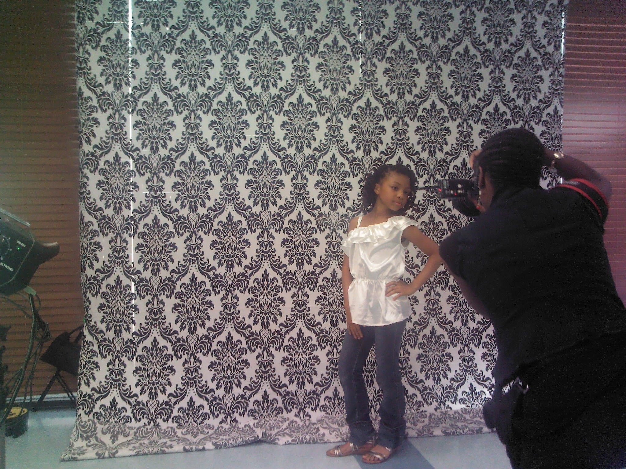 Child posing for a photo in front of a patterned backdrop, with a photographer taking the picture.