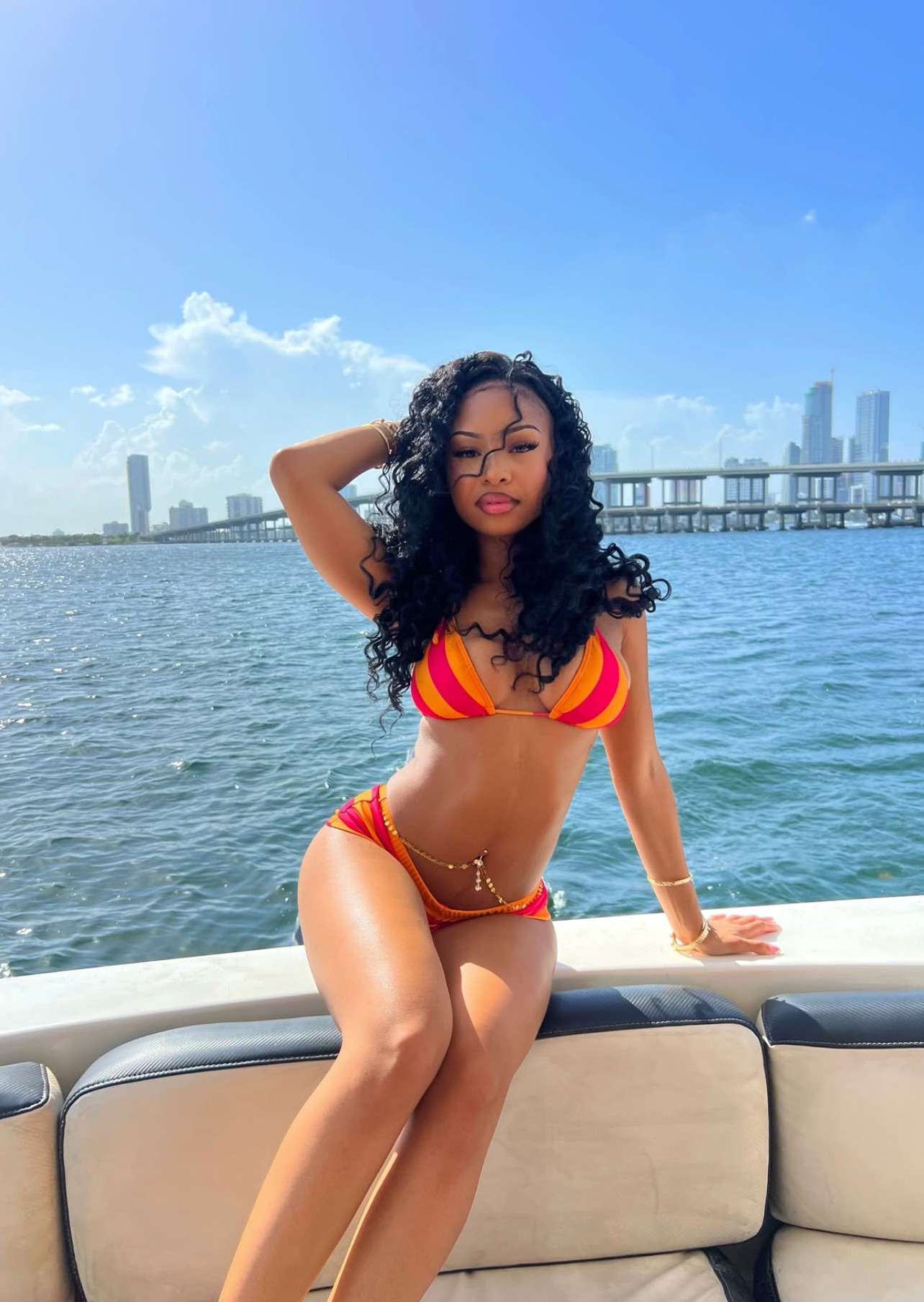 Woman in a red and yellow bikini sitting on a boat with water and city skyline in background