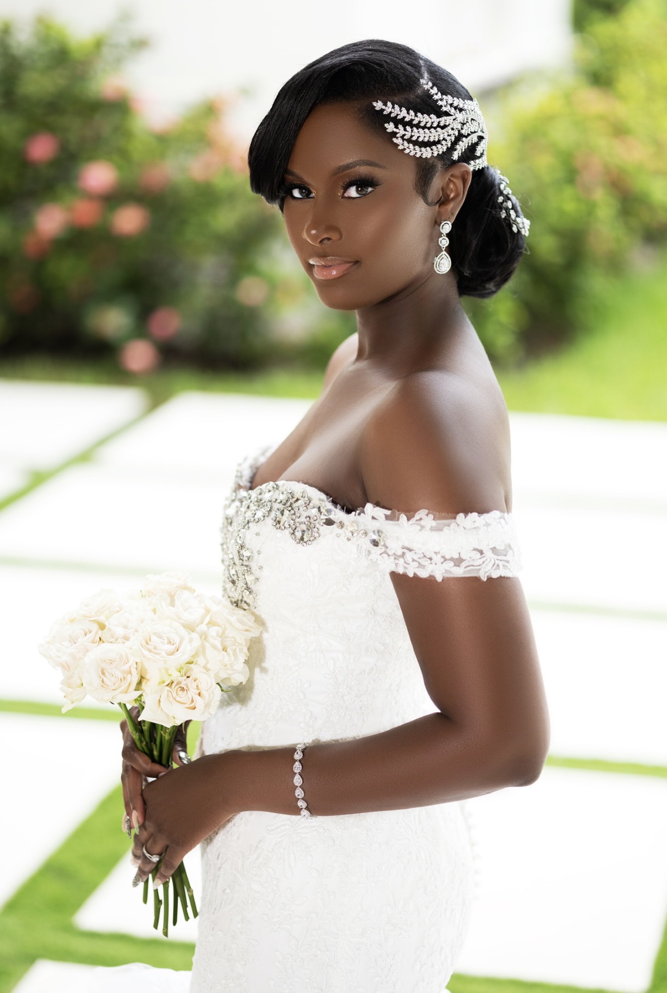 Young woman in wedding dress holding bouquet outdoors, with greenery and flowers in background.