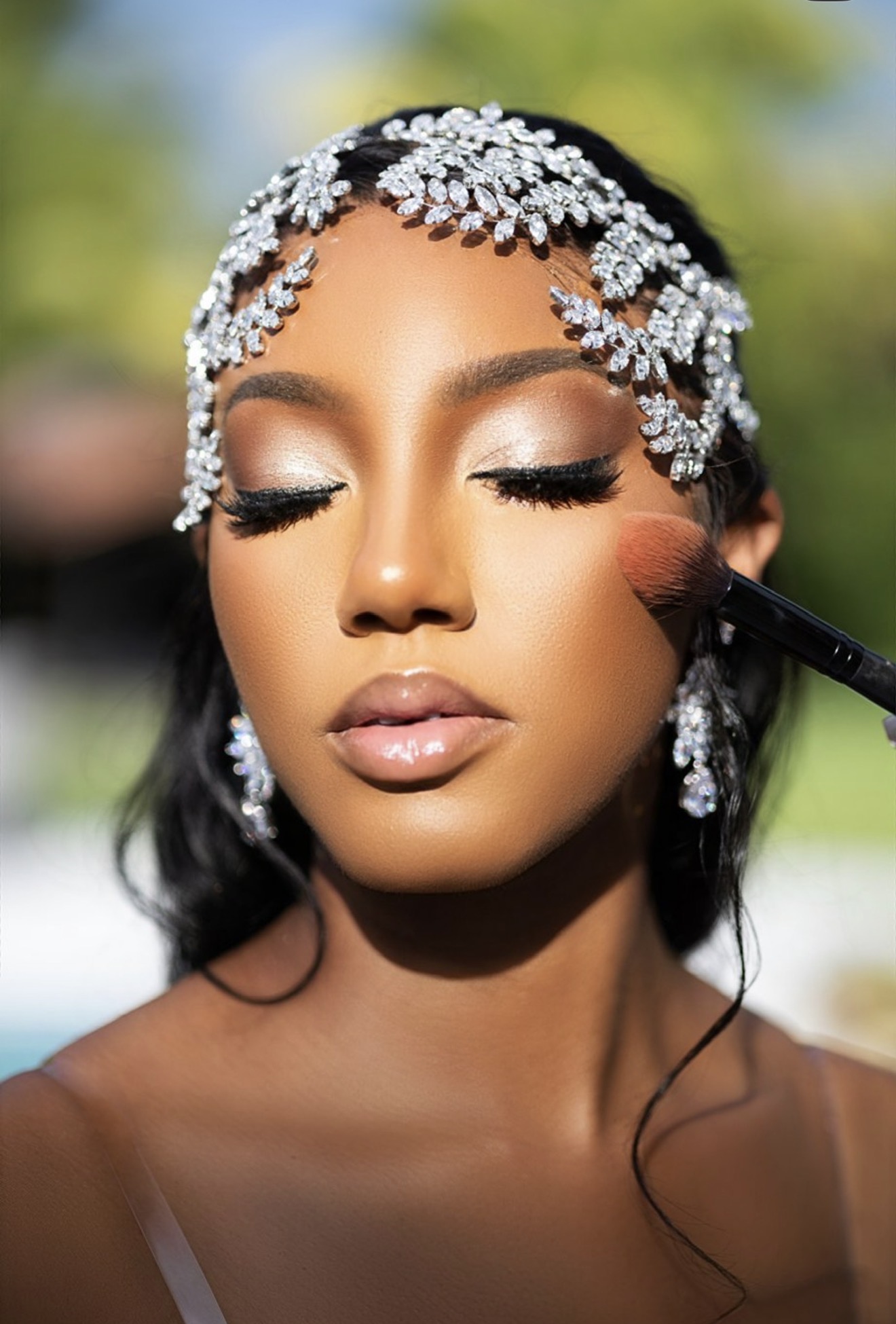 Woman with elaborate headpiece and makeup, eyes closed, outdoors with blurred background