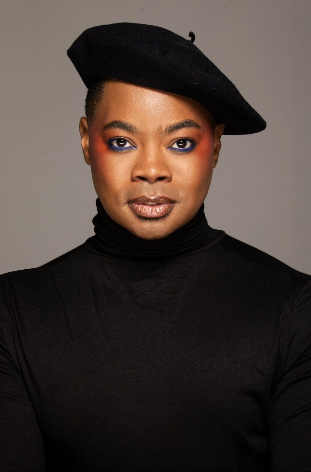 Woman wearing a black turtleneck and beret, looking directly at the camera with neutral expression.