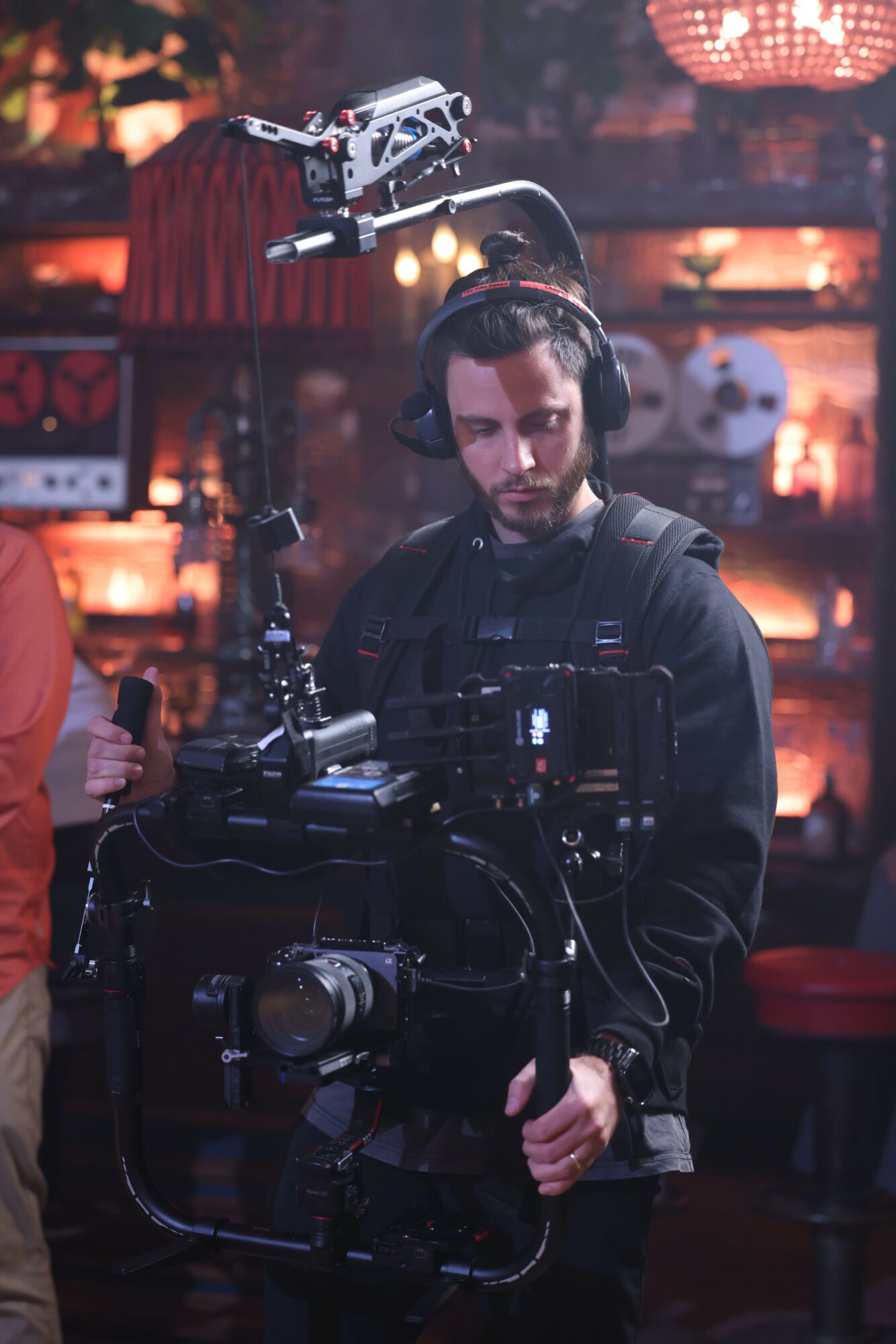 Person operating a camera on a film set with a cityscape background at night, illuminated by warm lights.