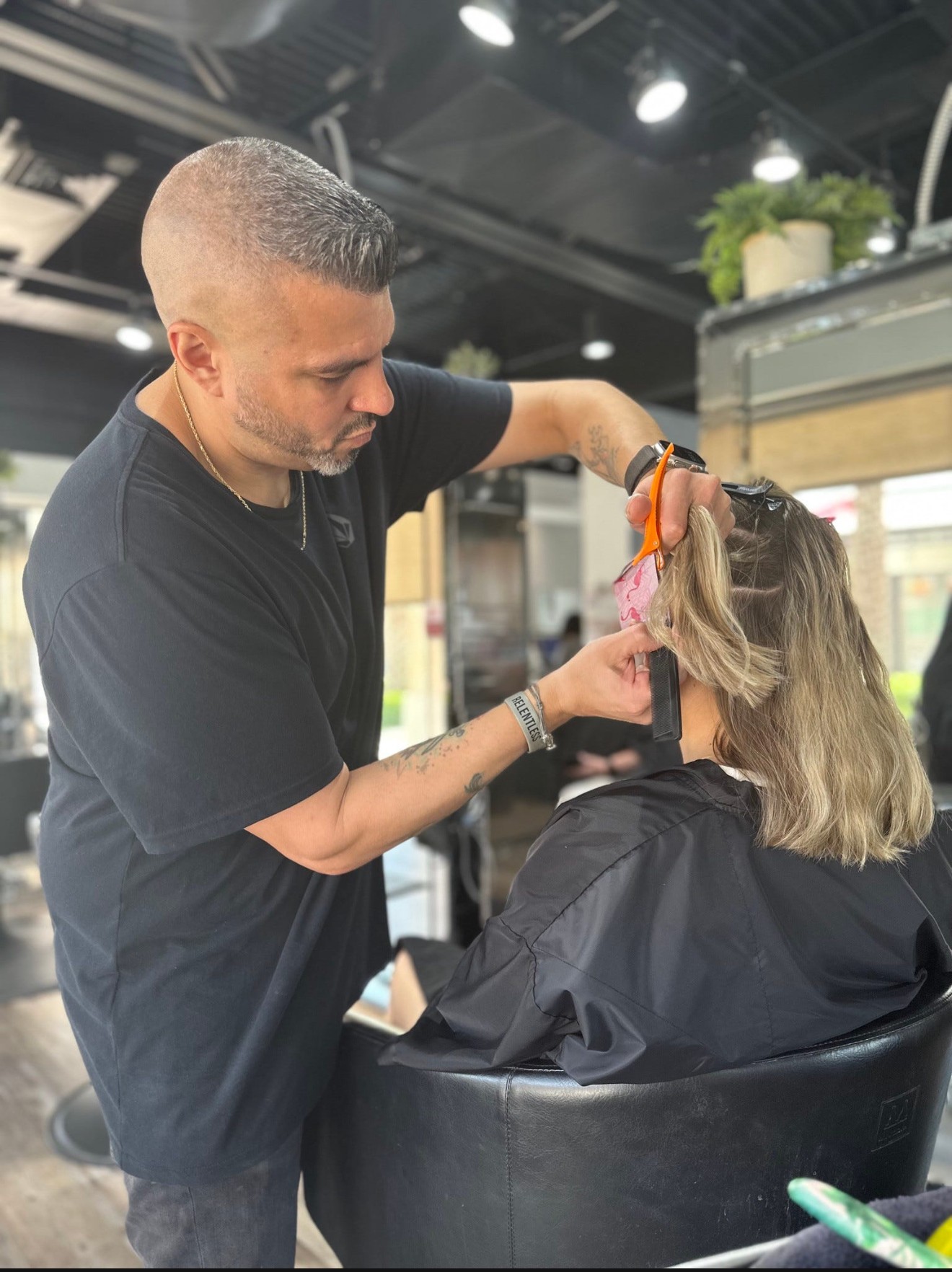Barber cutting a woman's hair in a salon, with hairdresser focused on styling, salon interior visible in background.