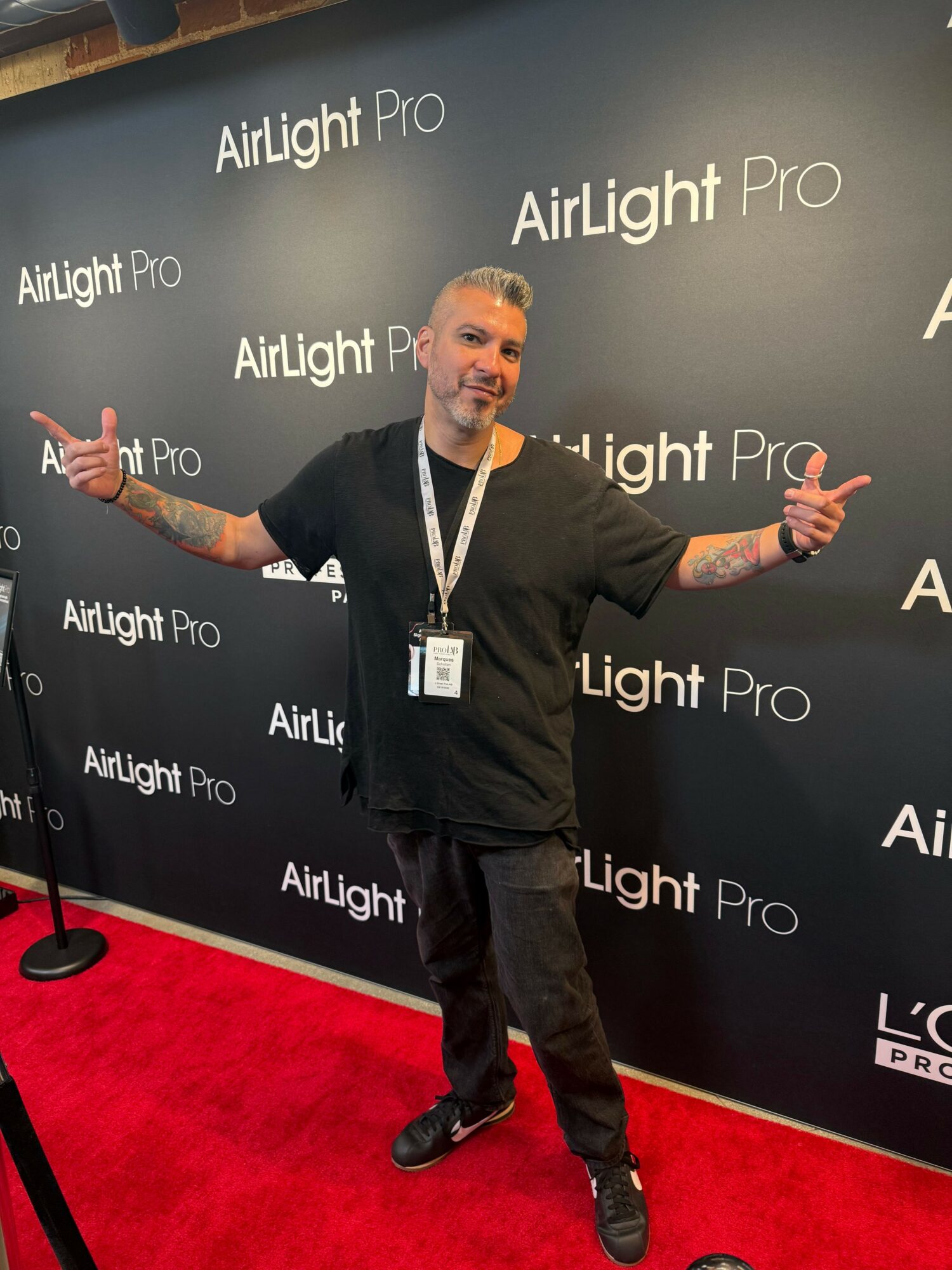 Person standing on red carpet, gesturing with hands, in front of black backdrop with 'Alight Pro' text.