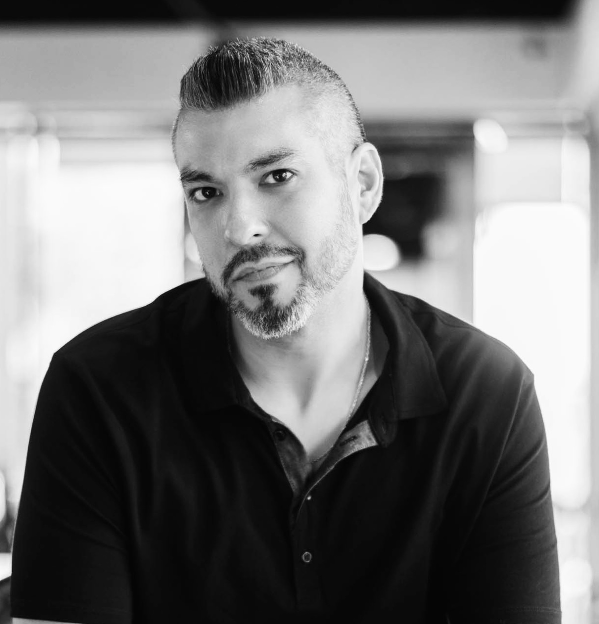 Man with short hair and beard wearing a dark polo shirt, looking at the camera, indoors.