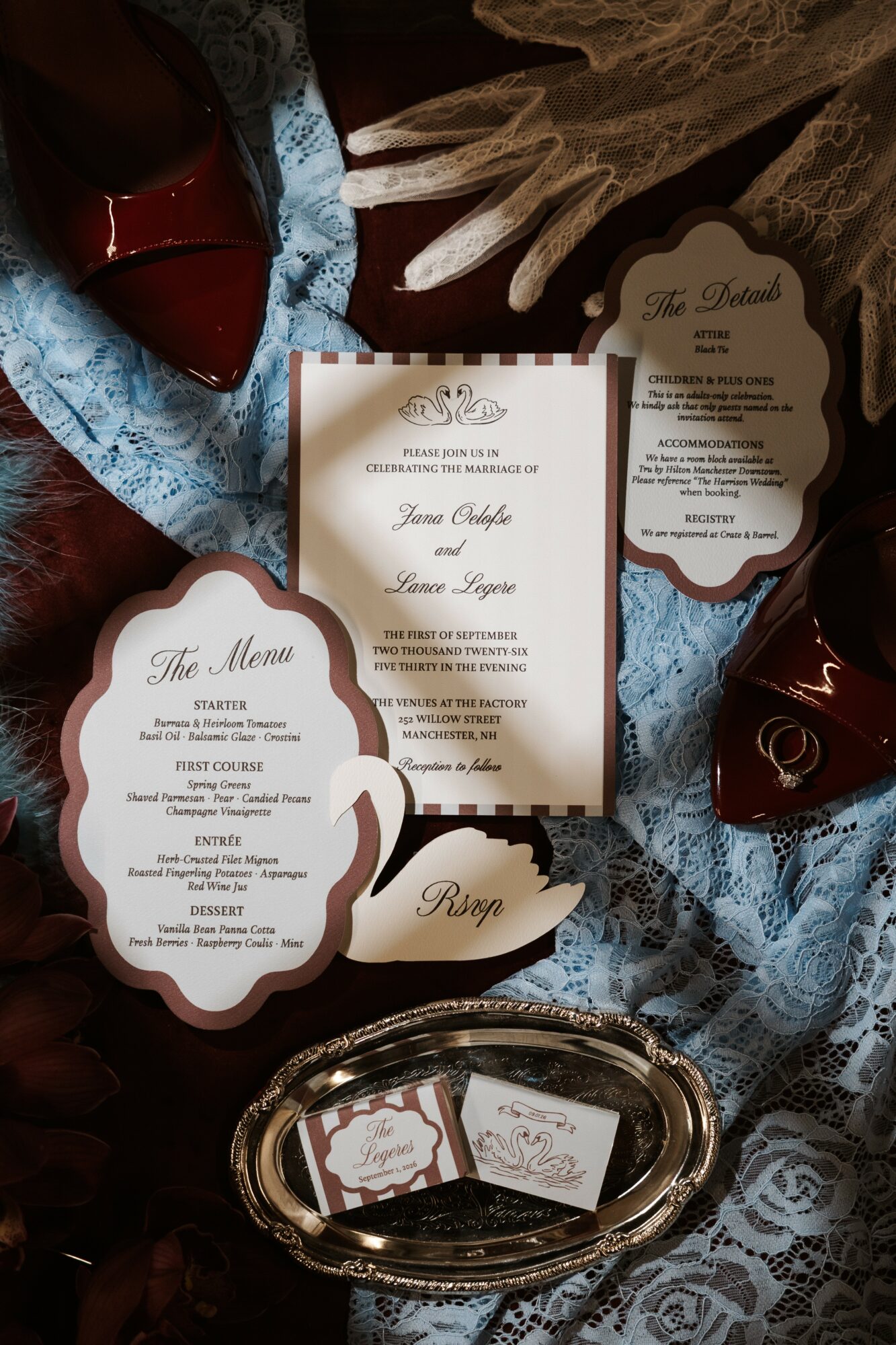 Wedding invitation, menu, and place card on lace tablecloth with red shoes and decorative items.