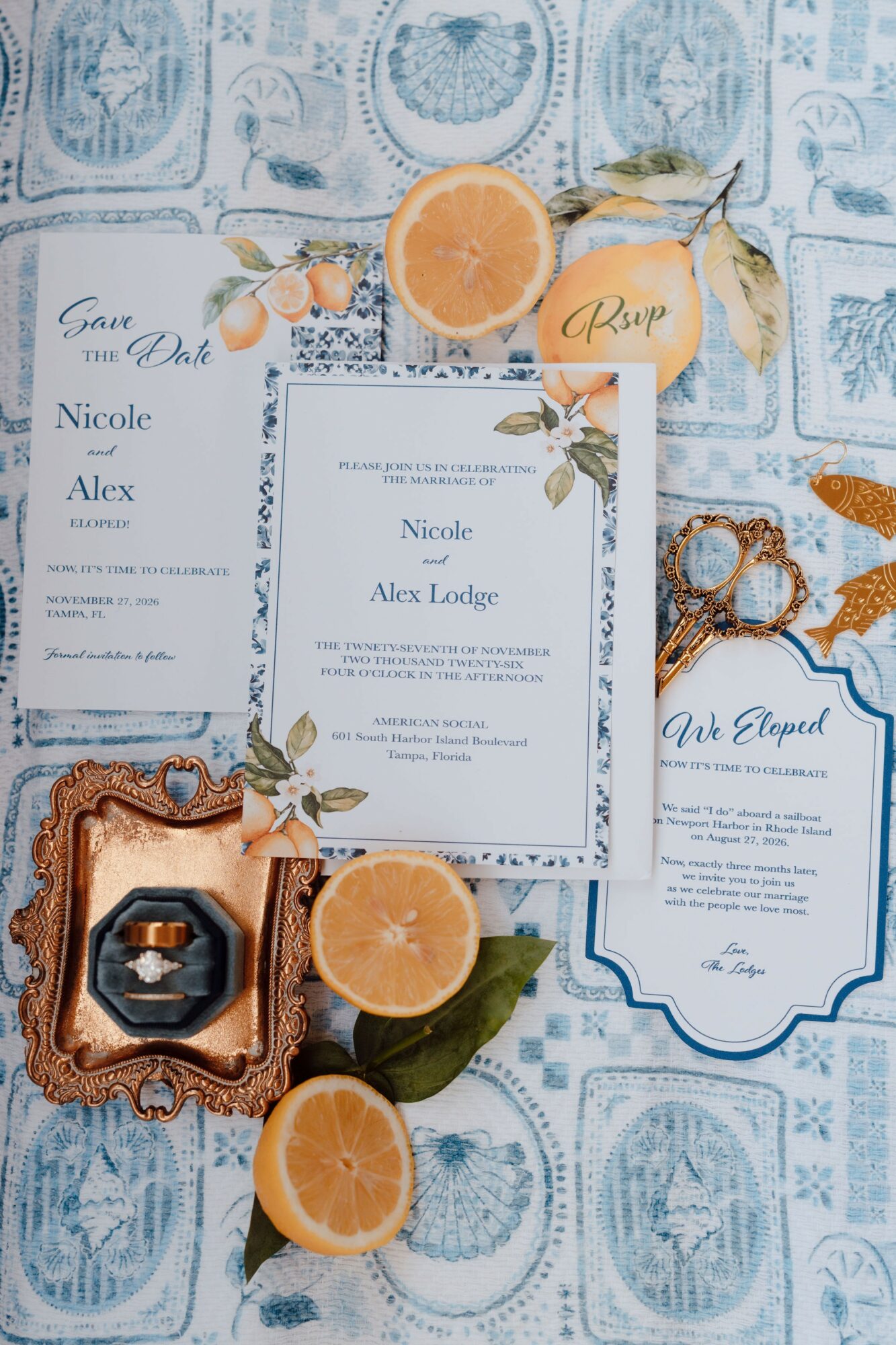Wedding invitation, orange slices, and decorative items on a blue patterned tablecloth.