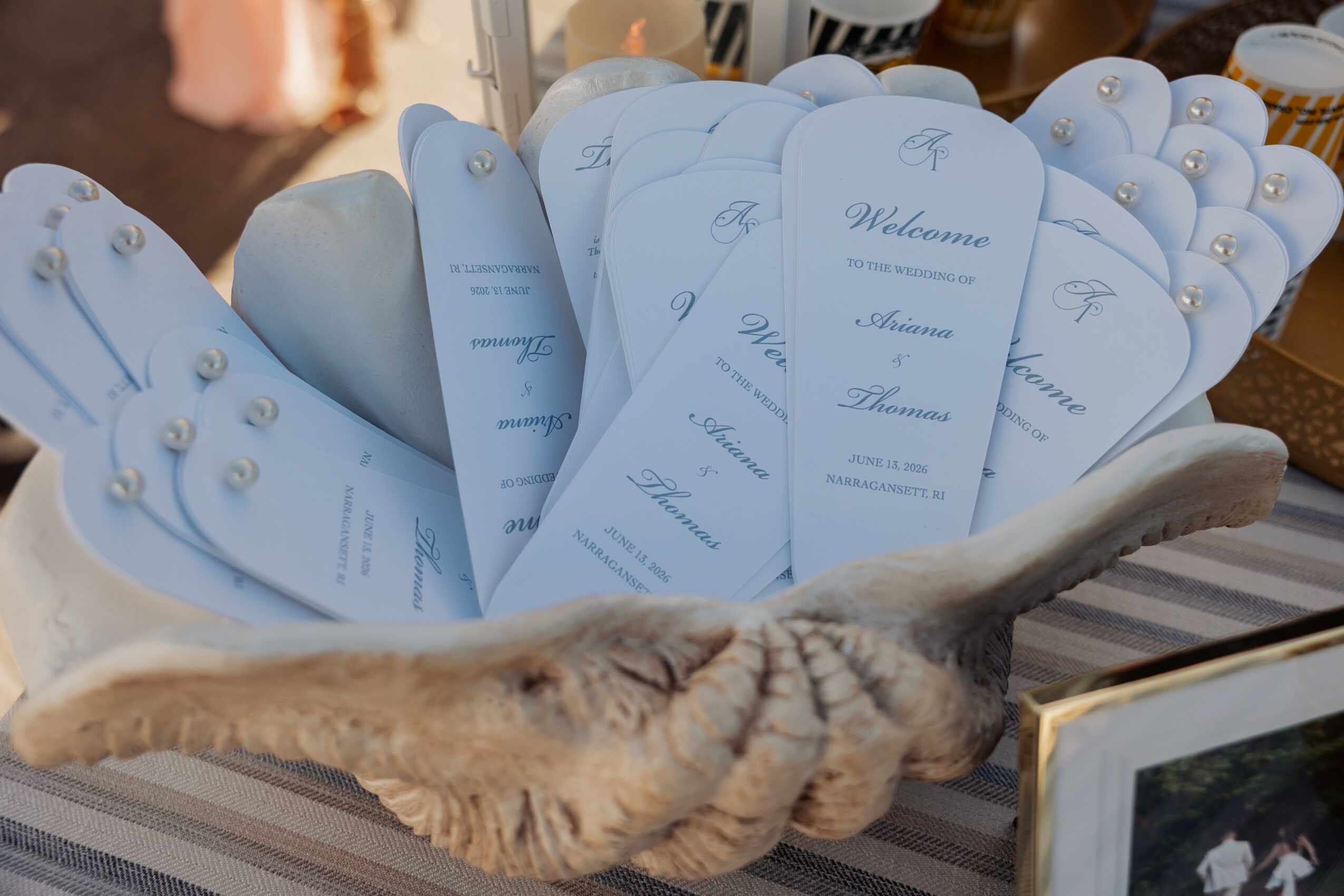 Decorative basket filled with wedding programs, with a feathered fan in front, on a striped surface.