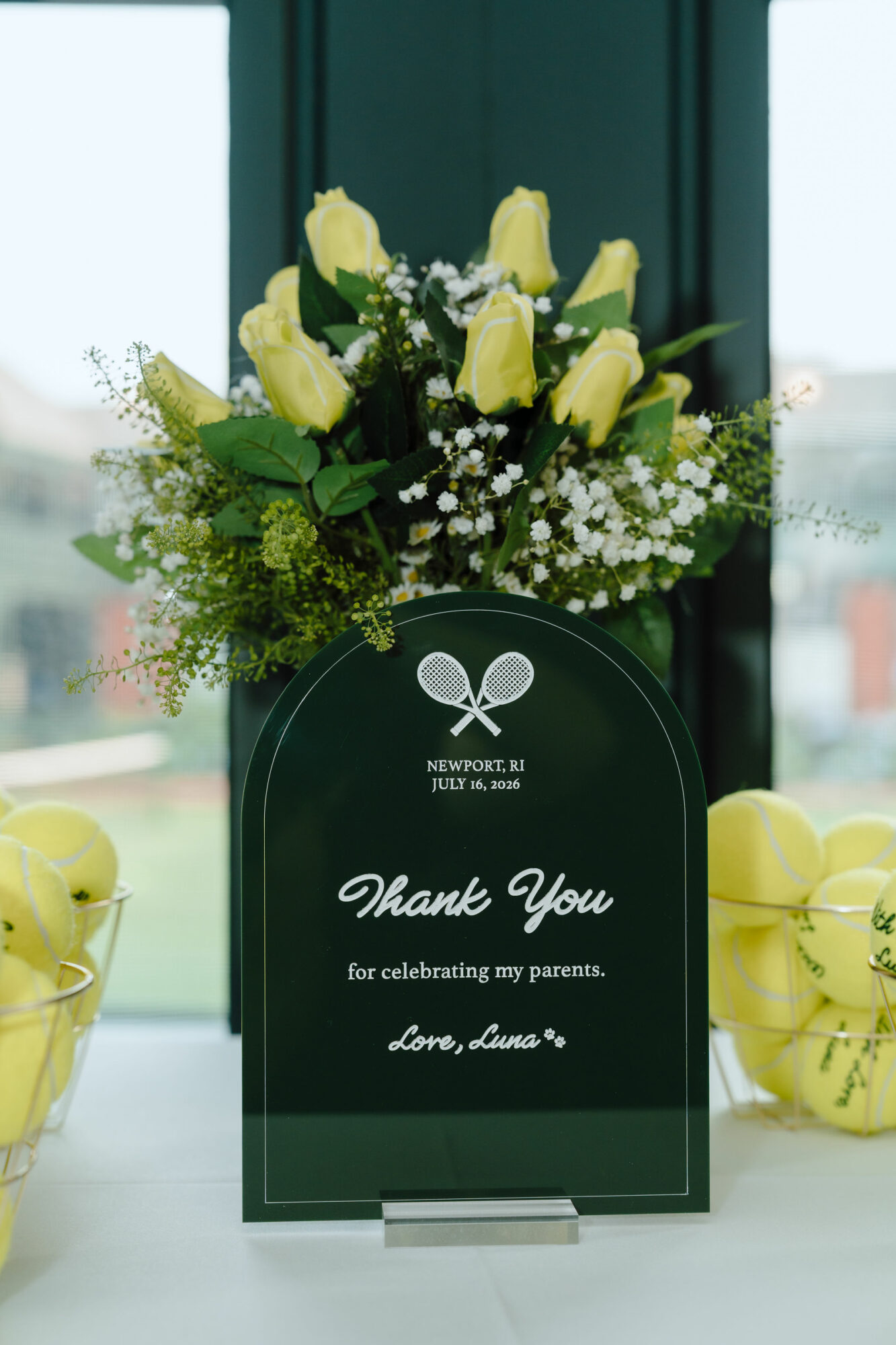 Yellow roses and white baby's breath in a dark green vase with a thank you message, surrounded by yellow apples.