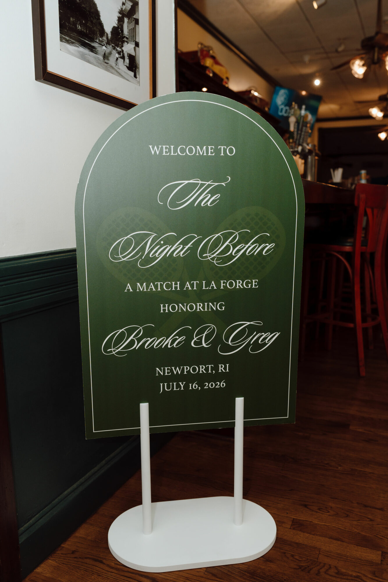Green arched sign with white text welcoming guests to a wedding event, with details about the couple and date.
