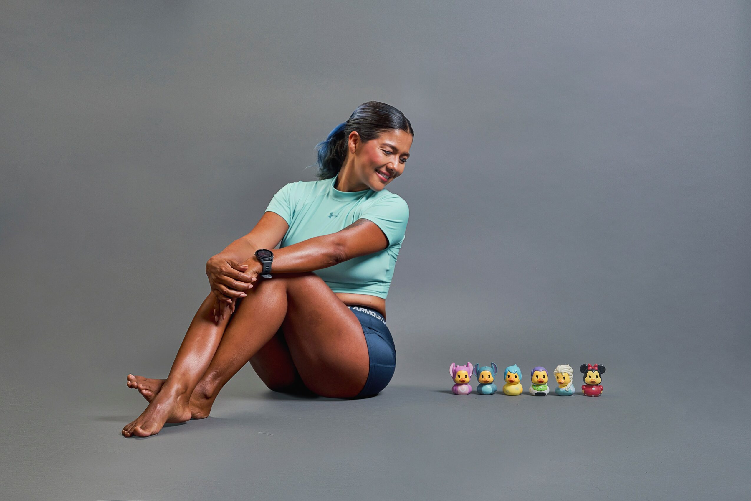 Woman sitting on the floor with legs crossed, smiling, with small colorful toys lined up beside her.