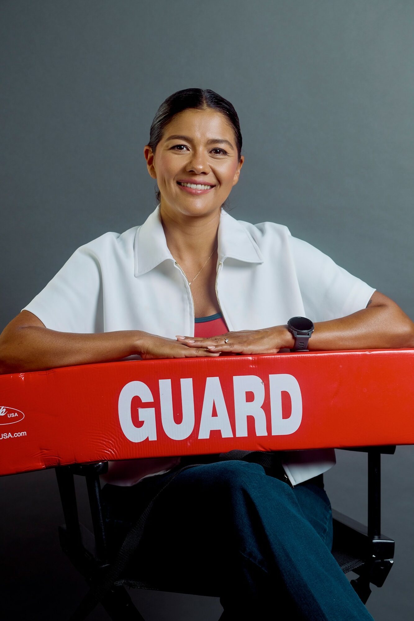 Smiling woman sitting behind a red guard desk with a gray background.