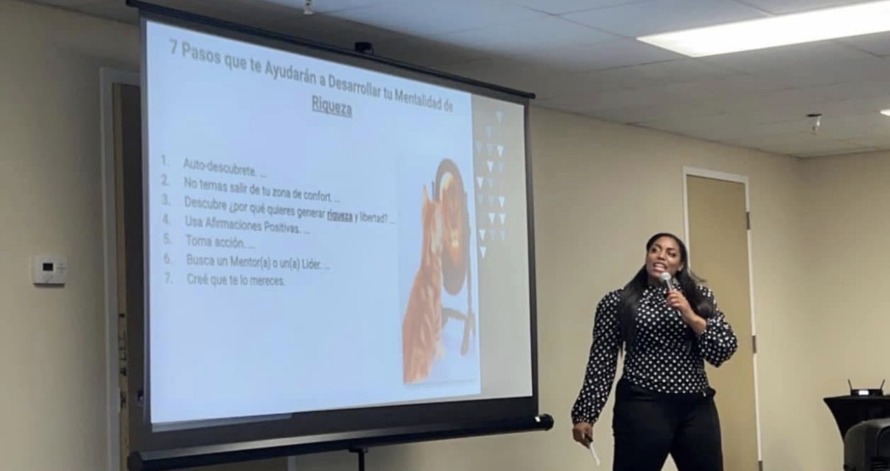 Person standing next to a presentation screen in a room, giving a talk or lecture.