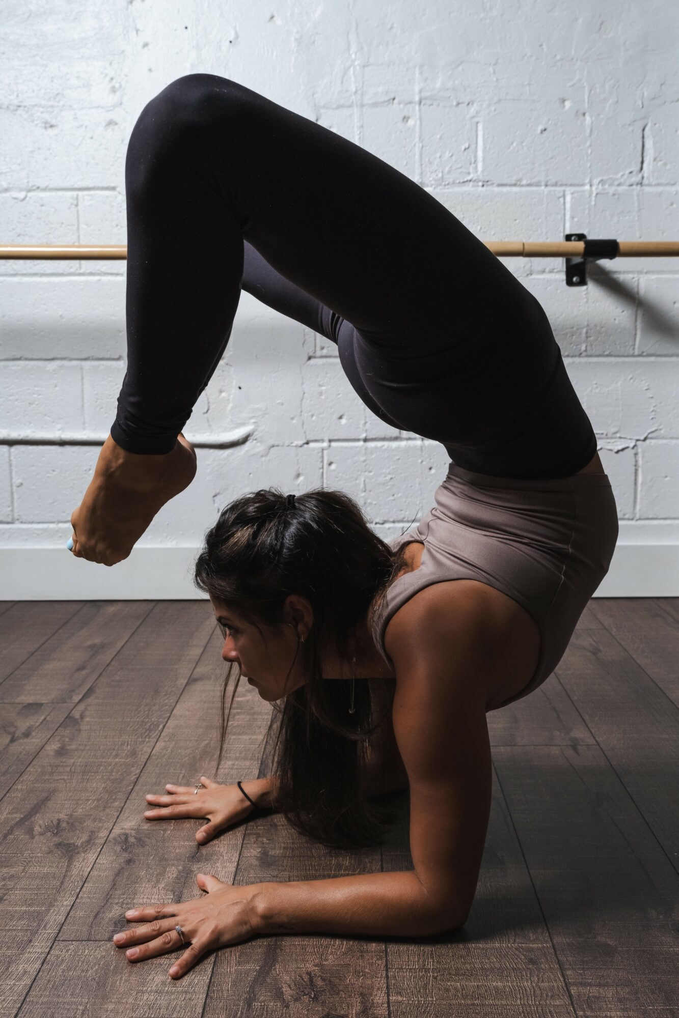 Woman performing a yoga pose balancing on her head and hands in a studio with a white brick wall.