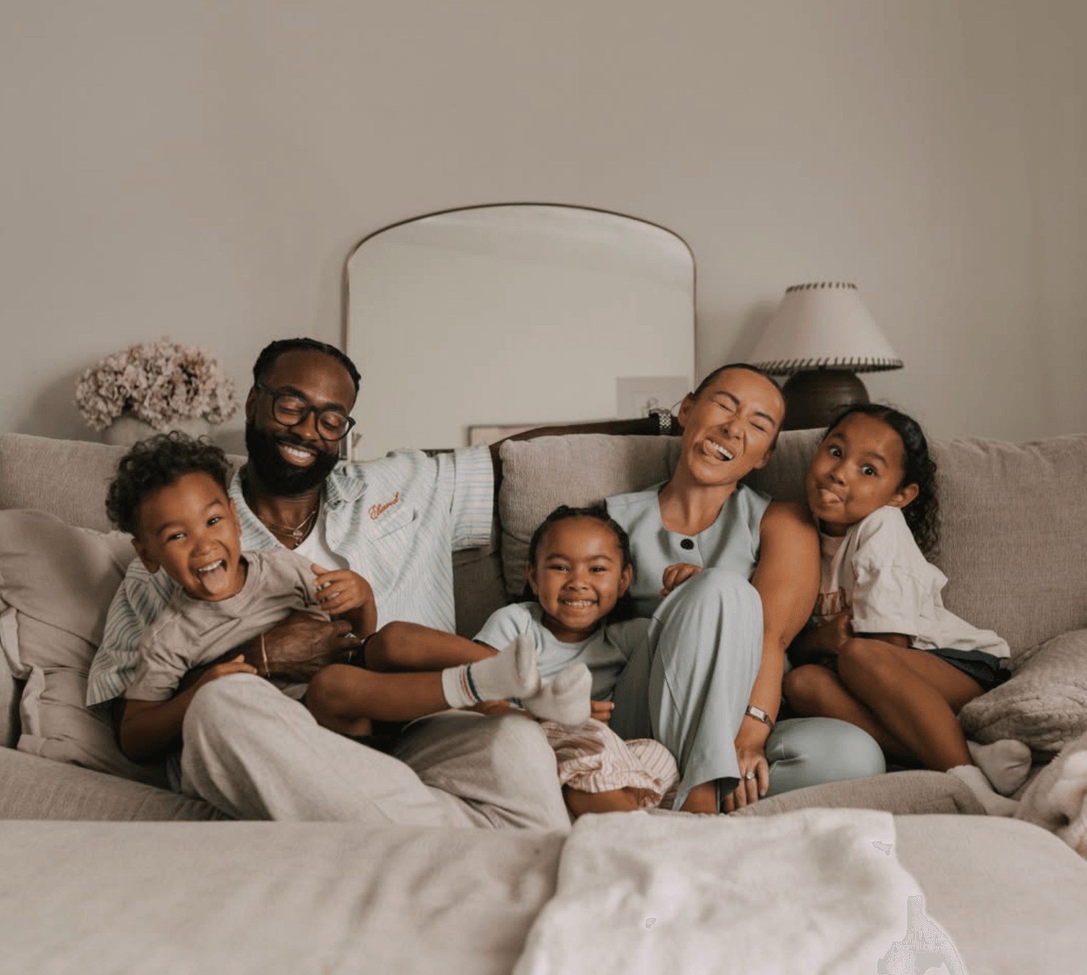 Family of six sitting on a sofa, smiling and laughing together in a living room.