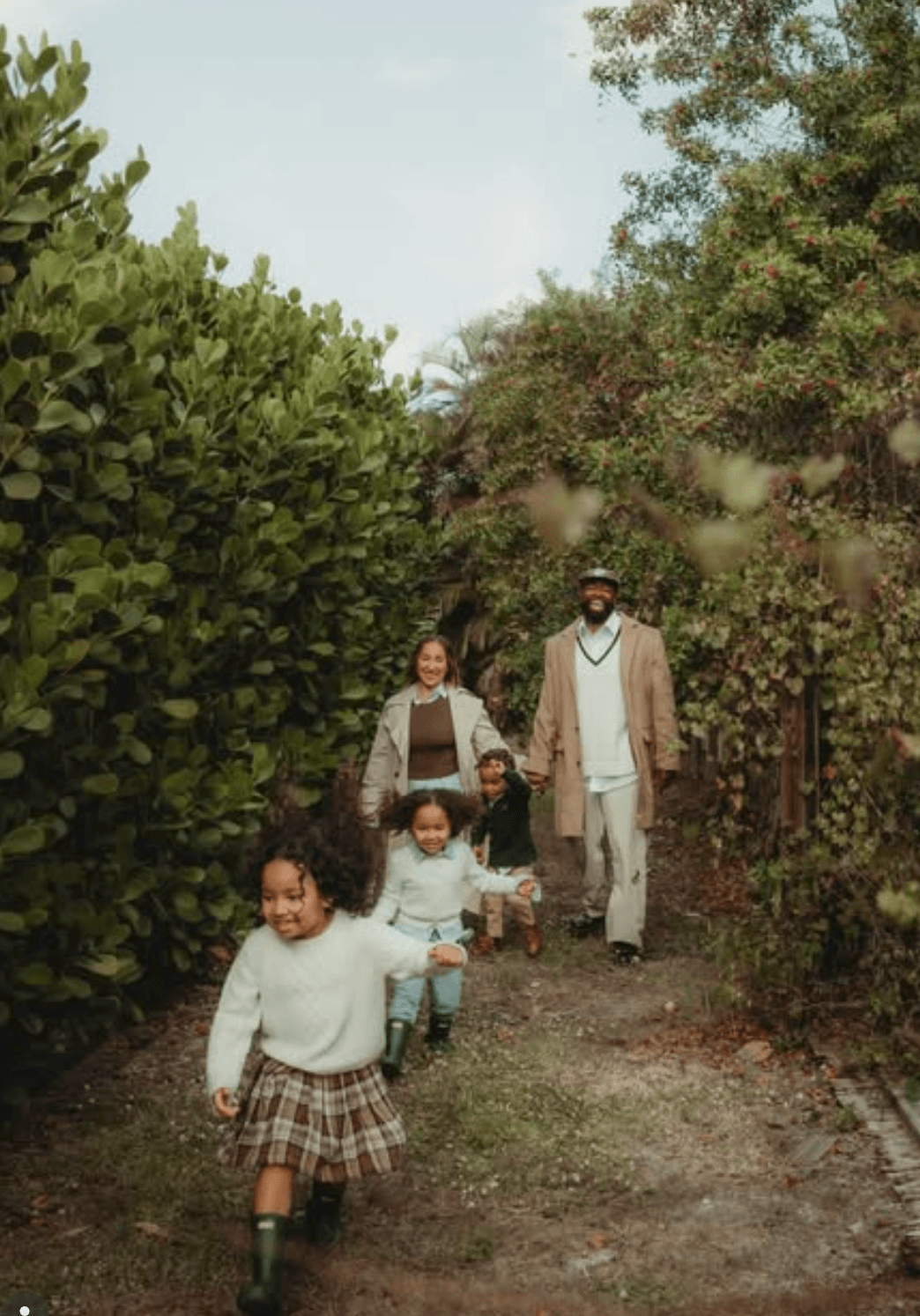 Group of children and two adults walking on a dirt path surrounded by trees and greenery.