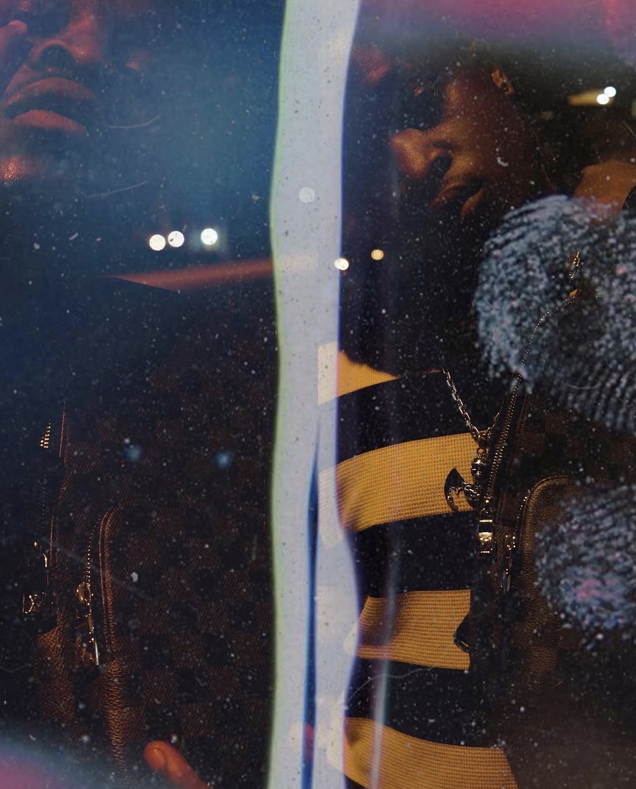 Two people are reflected in a glass surface with city lights in the background at night.