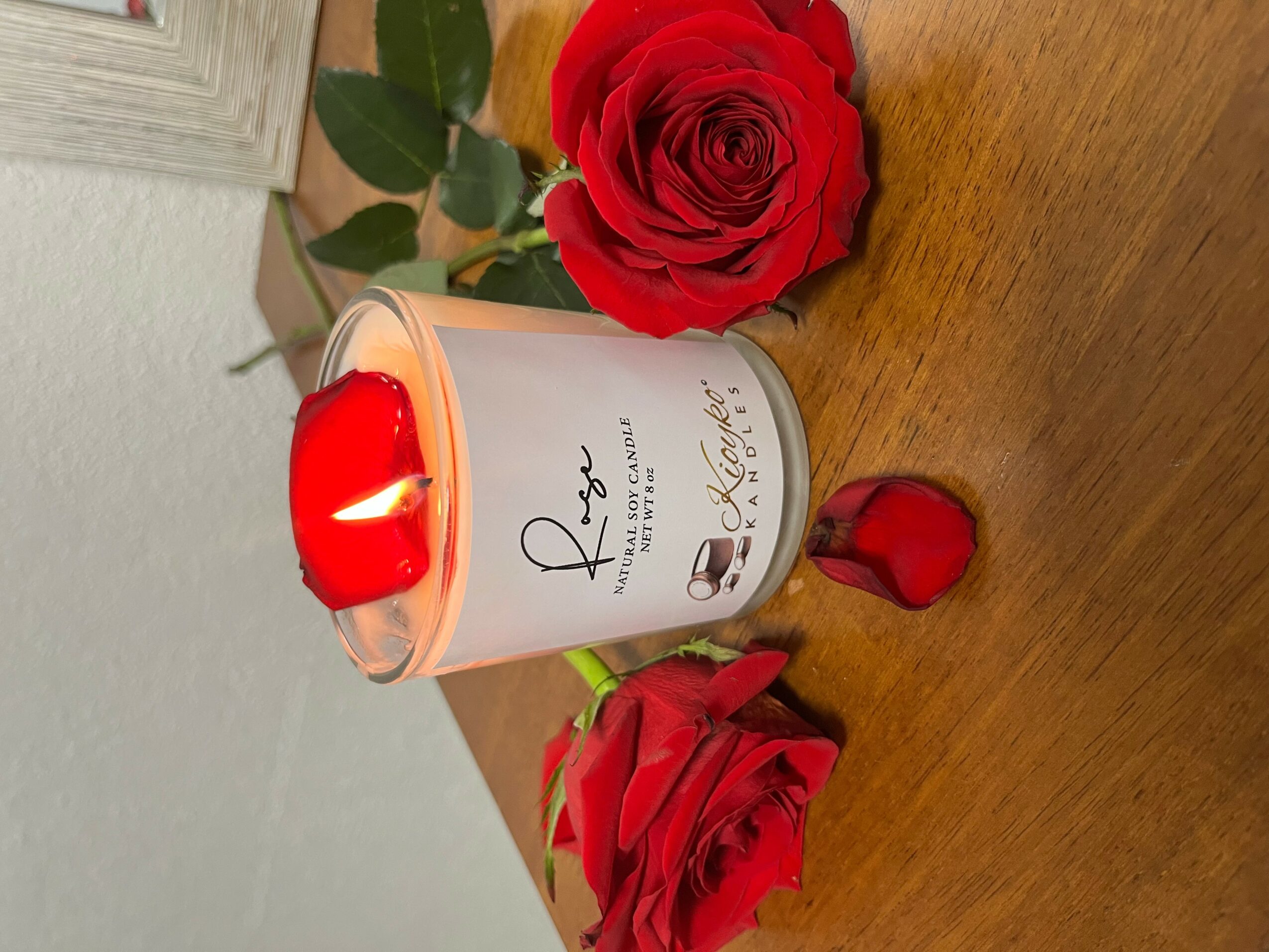 Red roses and a candle with a rose design on a wooden surface.