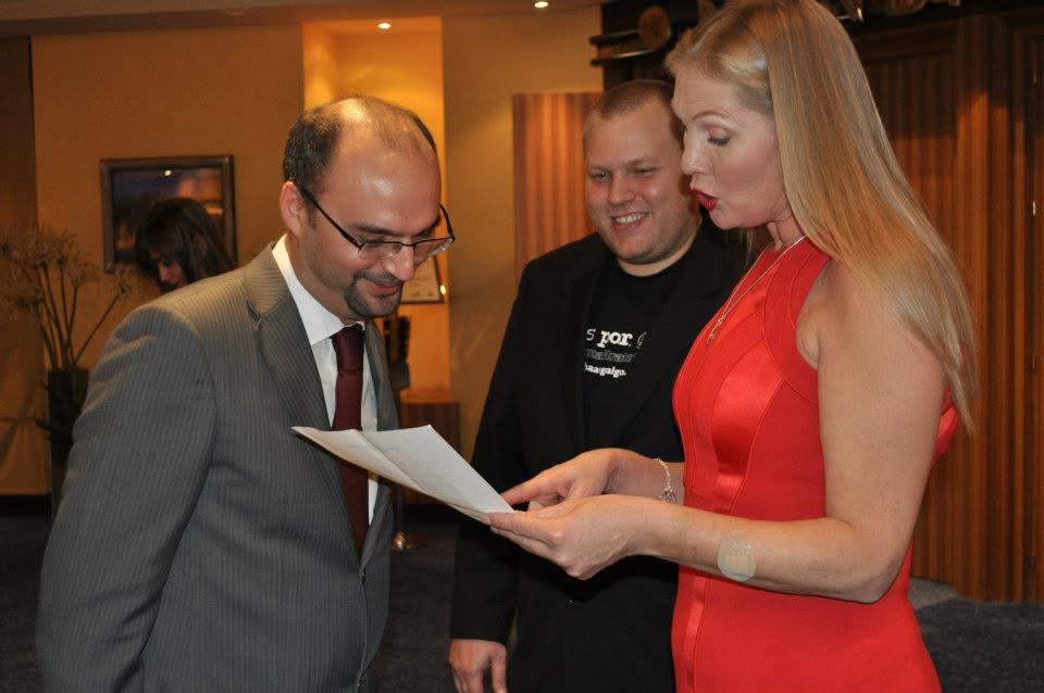 Three people, two men and one woman, look at a document together indoors, smiling and engaged.